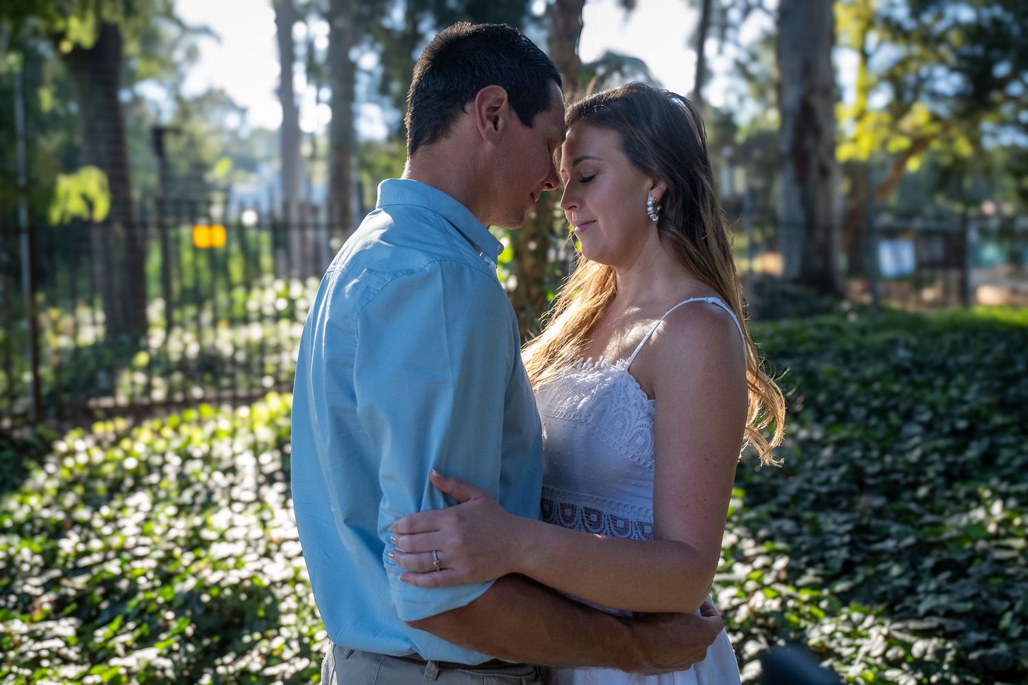 Couple sharing a tender forehead-to-forehead embrace in a sunlit garden with ivy in the background.