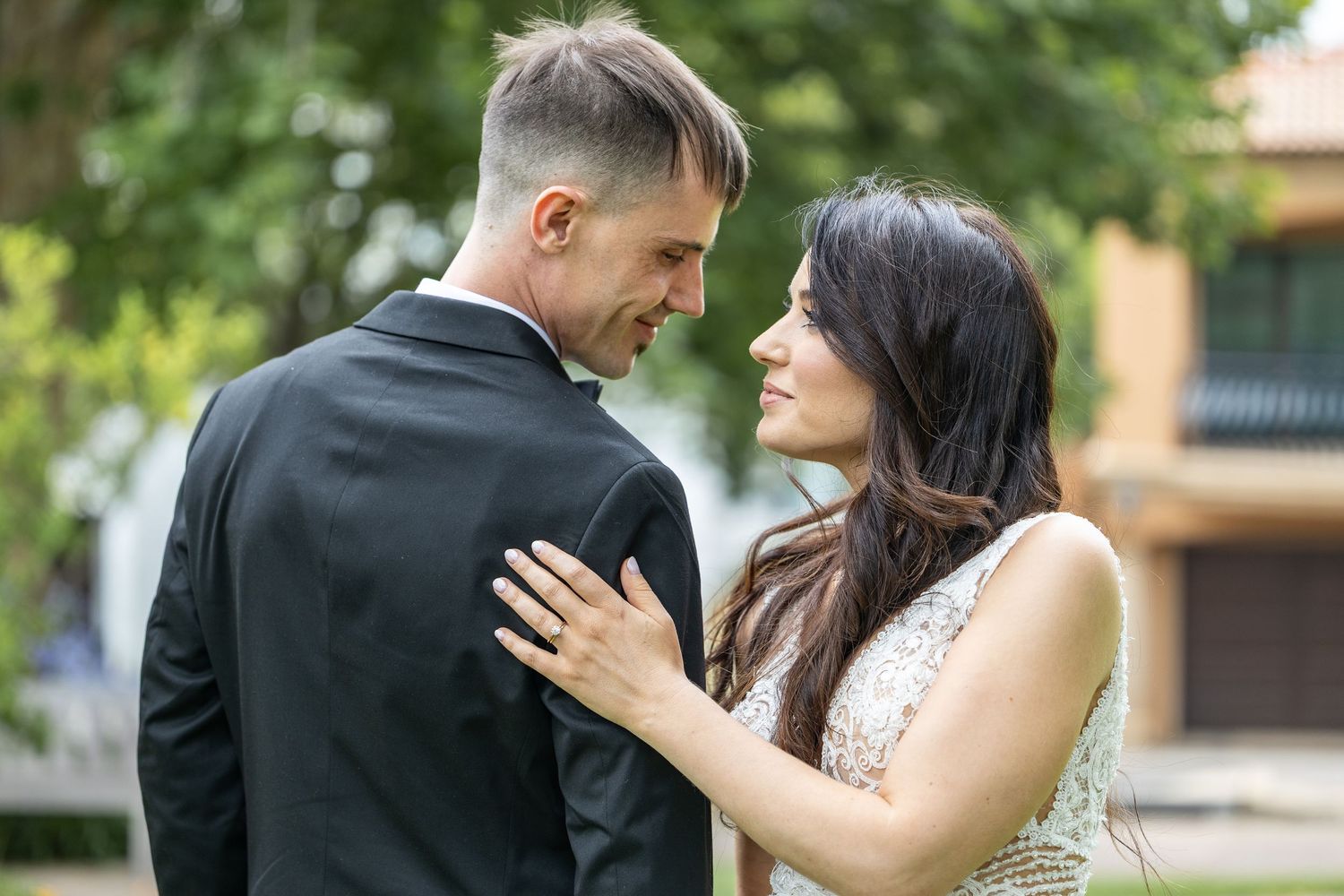 Bride and groom gazing into each others eyes while standing face to face in sunny park.
