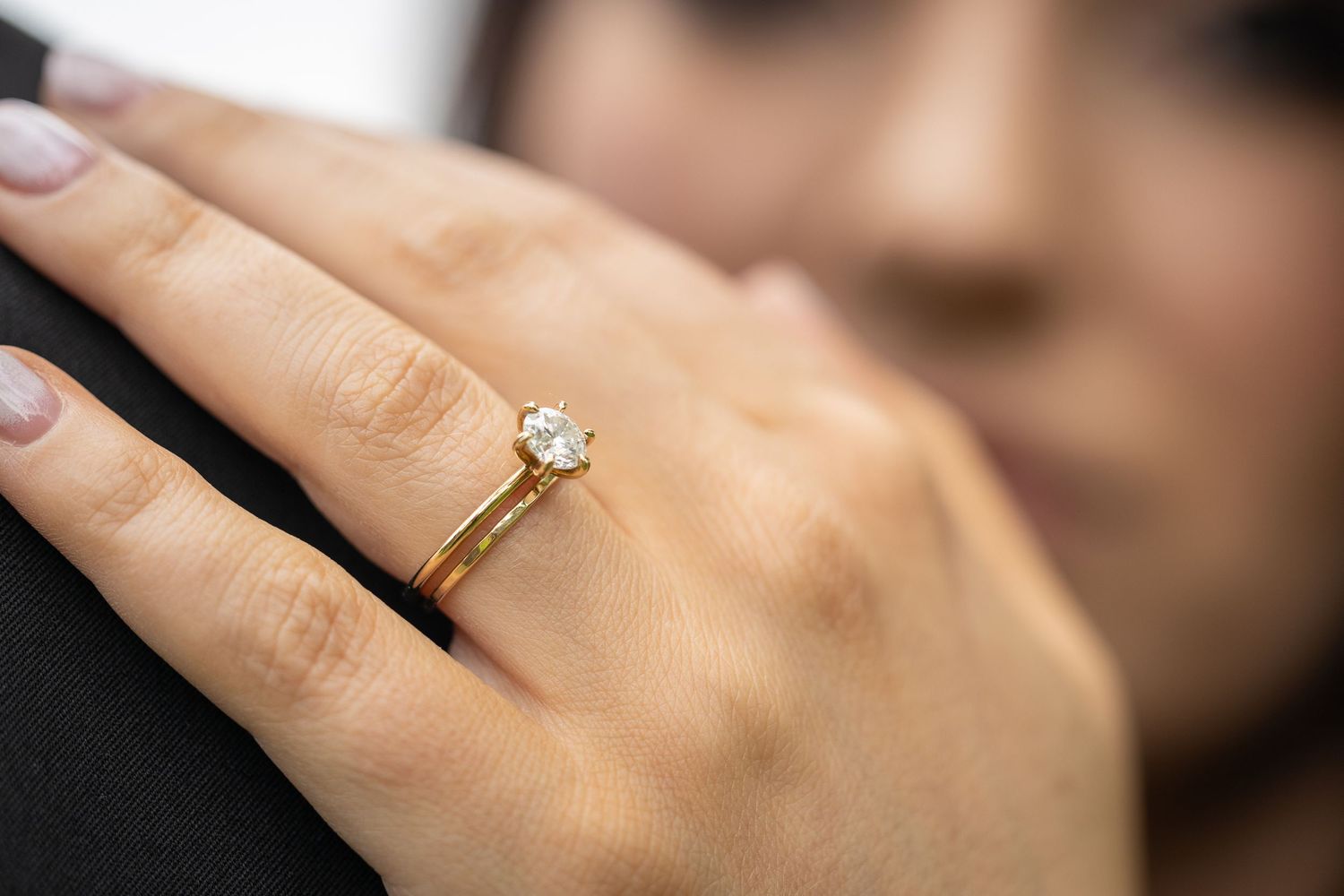 Close-up of elegant gold solitaire diamond engagement ring on brides finger against dark background.