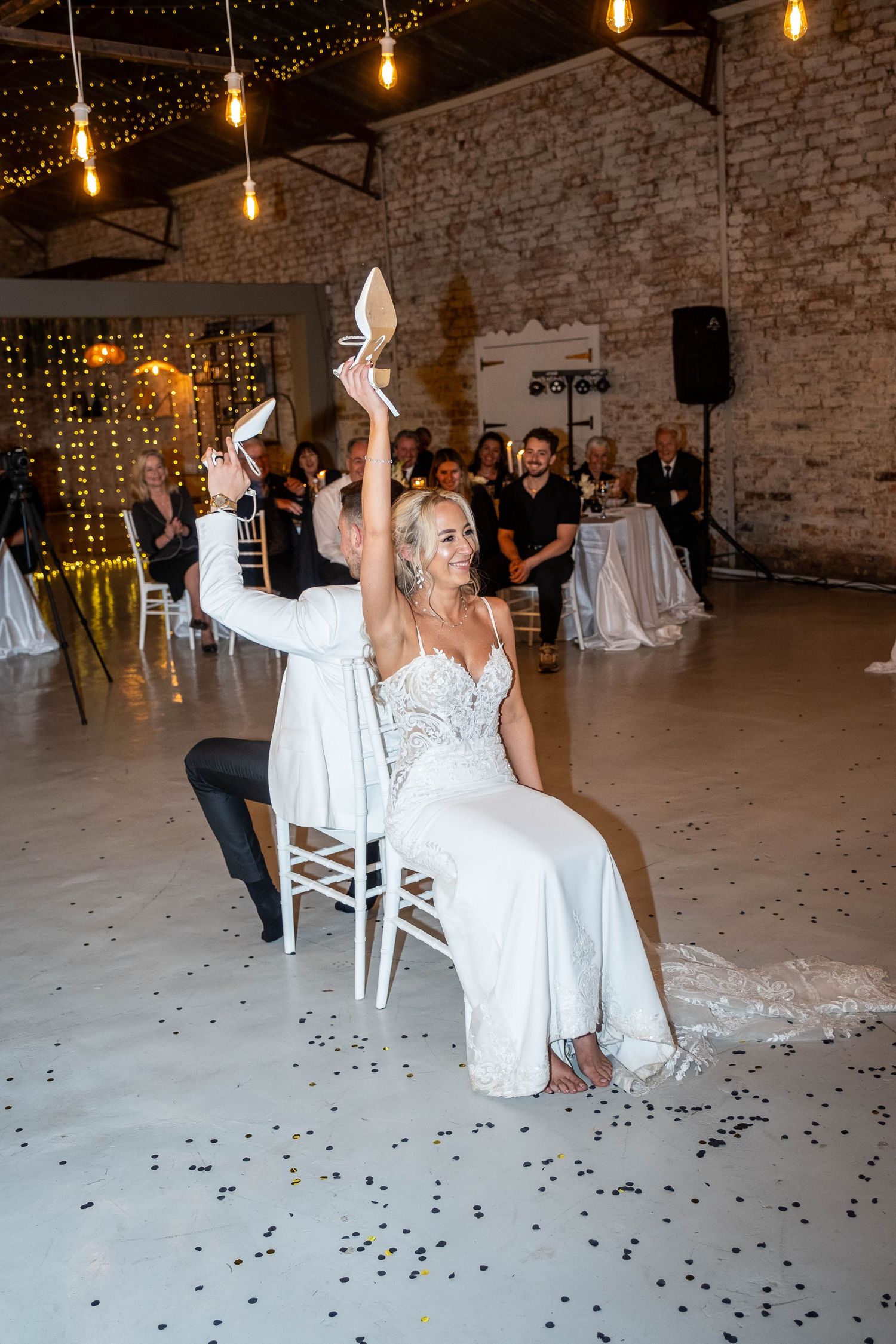 Laughing bride holds up high heel shoe during fun wedding shoe game at barn reception.