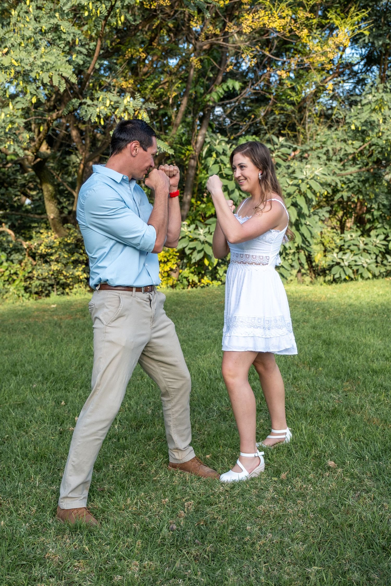 Playful couple pretending to box each other in a lush green park.