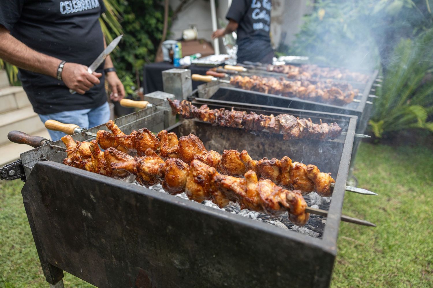 Outdoor BBQ catering with skewers of grilled chicken cooking over charcoal at wedding reception.