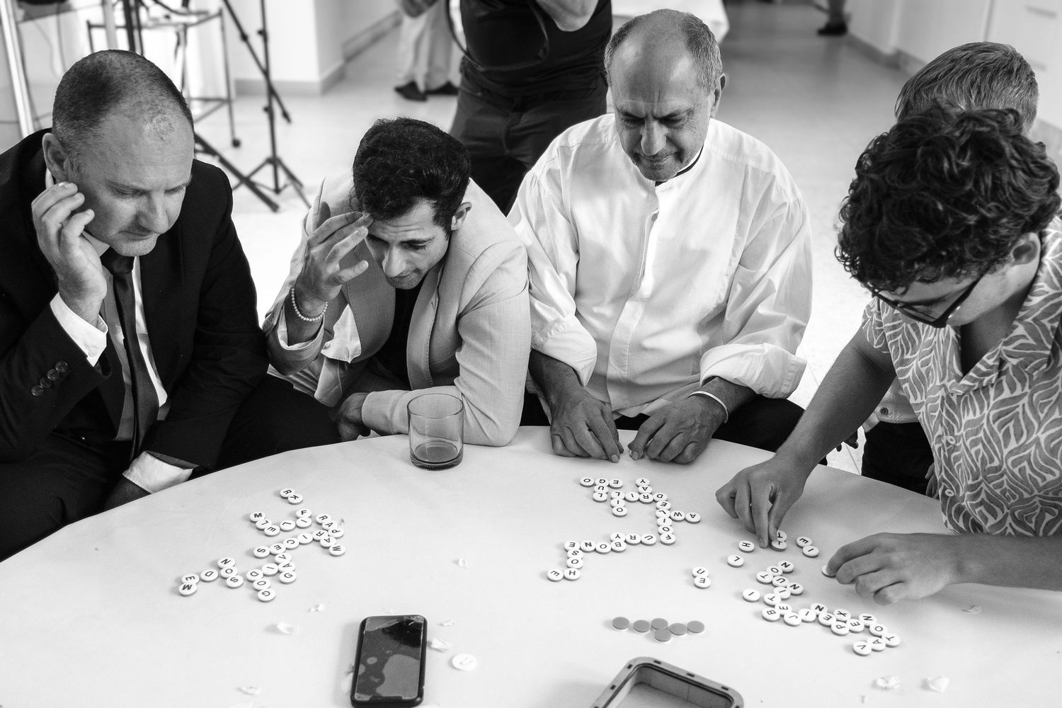 Black and white photo of four men playing dominoes at a round table during a wedding reception.