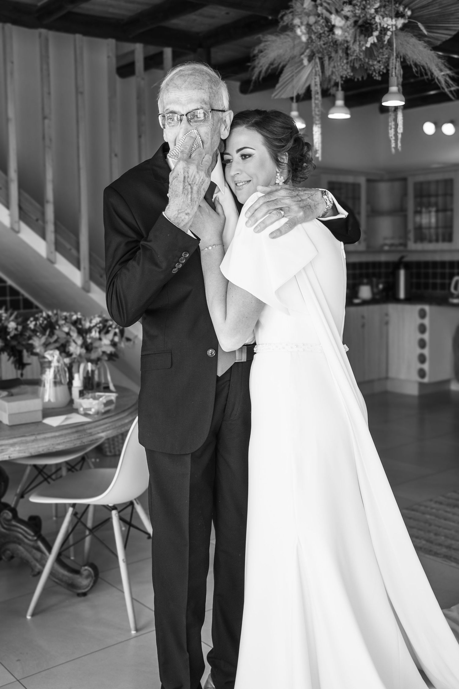 Black and white photo of an emotional father in a suit embracing his bride daughter before the wedding ceremony.
