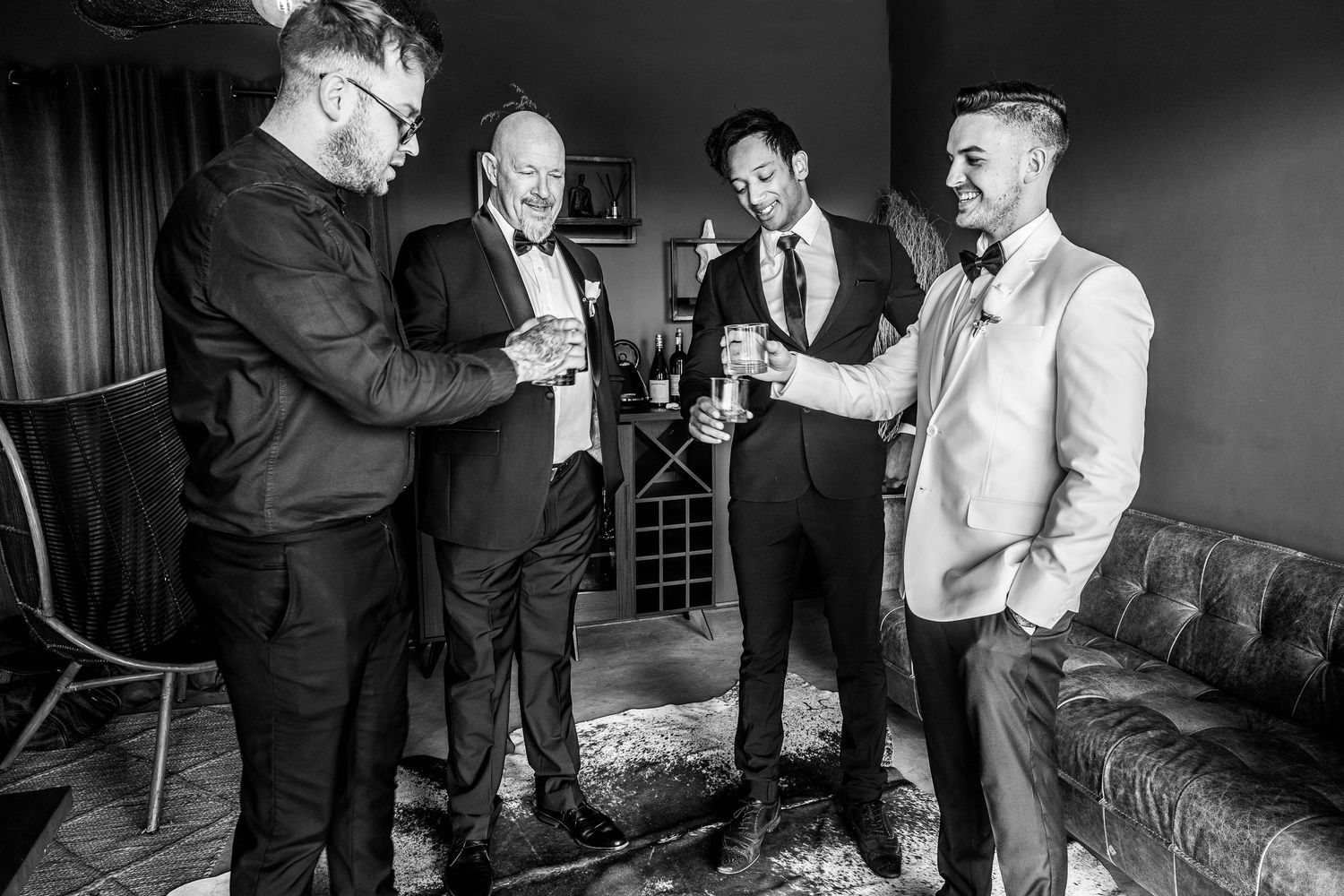 Four groomsmen in formal attire share a celebratory toast with champagne before the wedding ceremony.