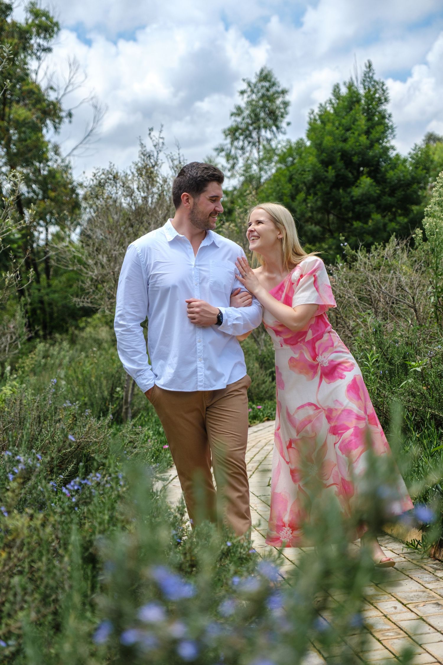 Romantic couple walking together on a wooden path surrounded by greenery.