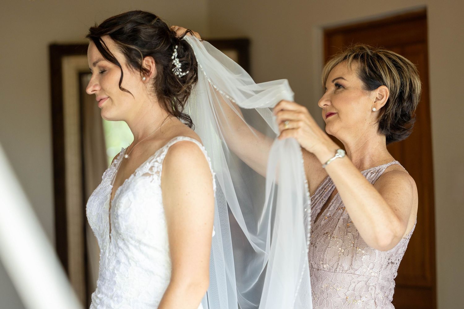 Mother of the bride helping adjust the wedding veil on the bride in a lace wedding dress.