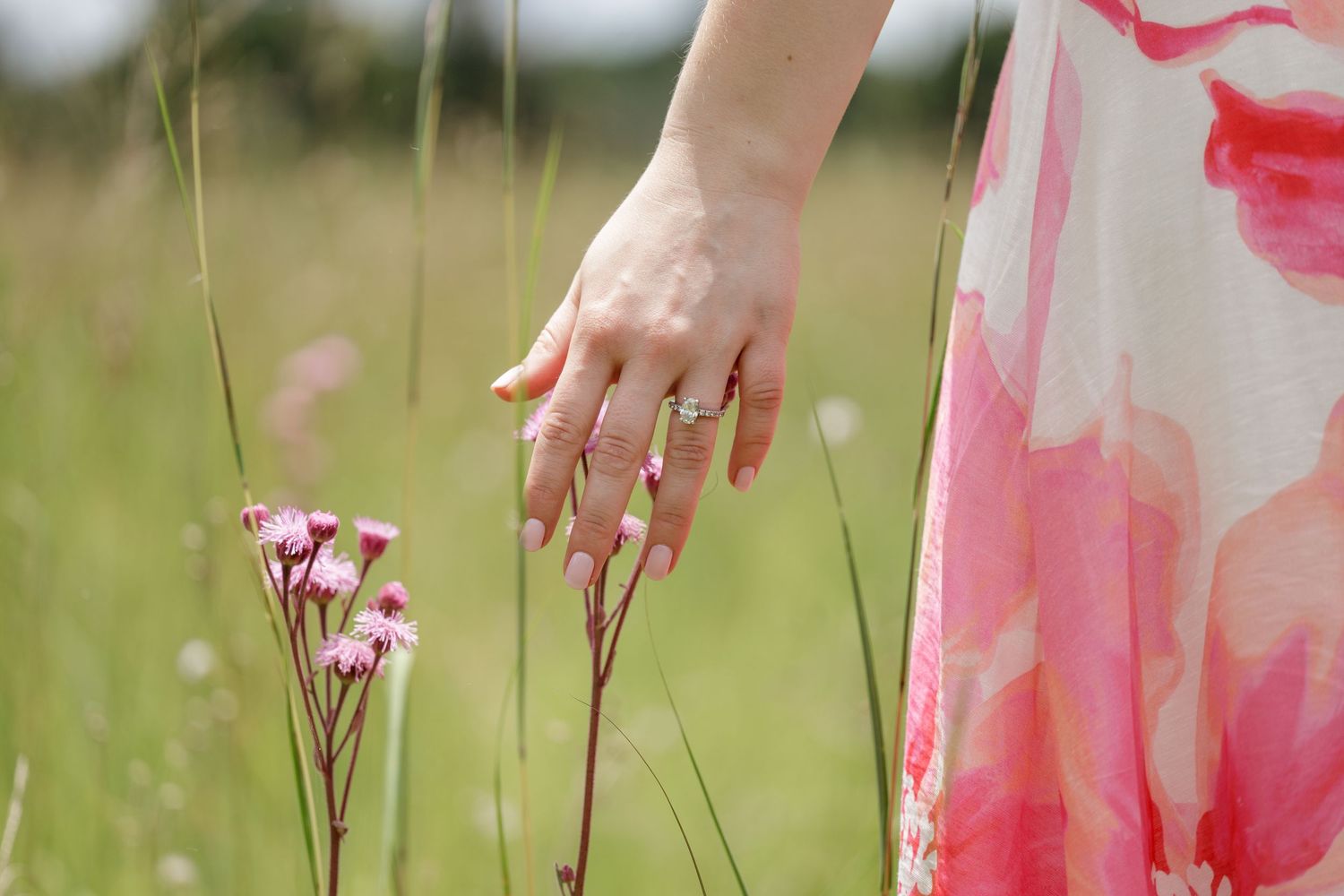 Close-up of a woman's hand with an engagement ring touching pink wildflowers.