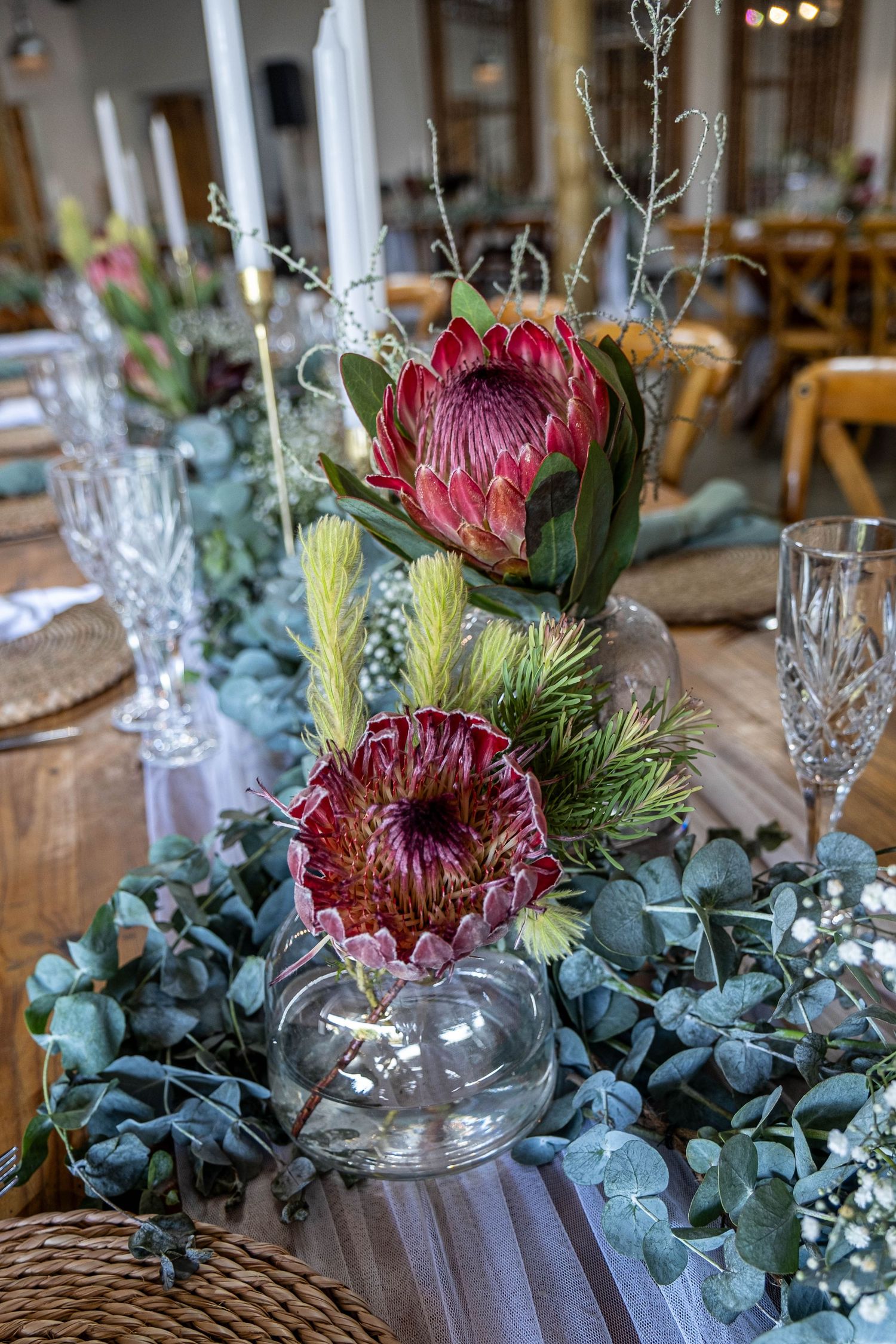 Elegant wedding table centerpiece with King Protea flowers, eucalyptus and crystal glasses.