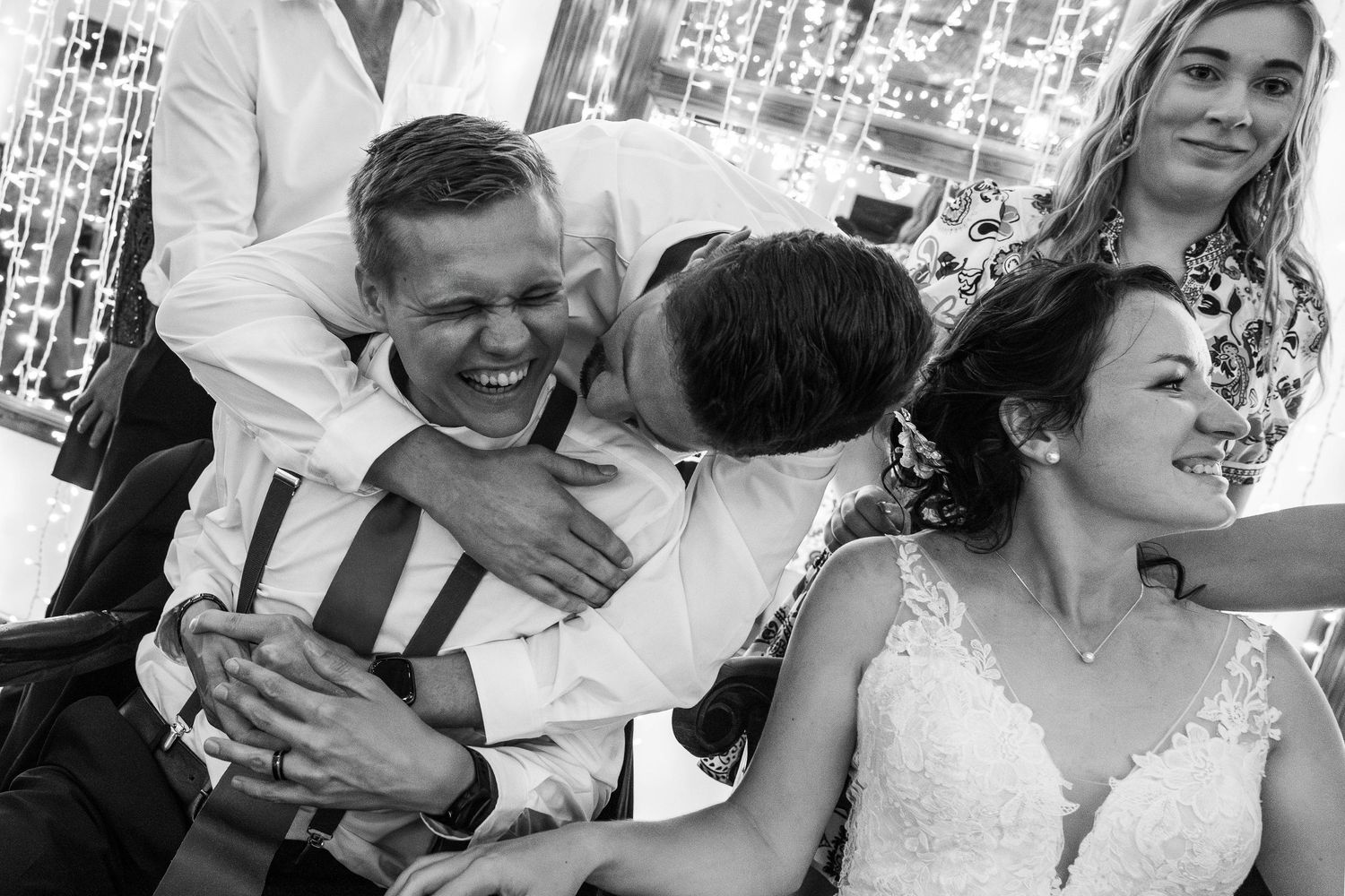Groom laughs joyfully as a guest hugs him warmly during a lively black and white wedding reception.