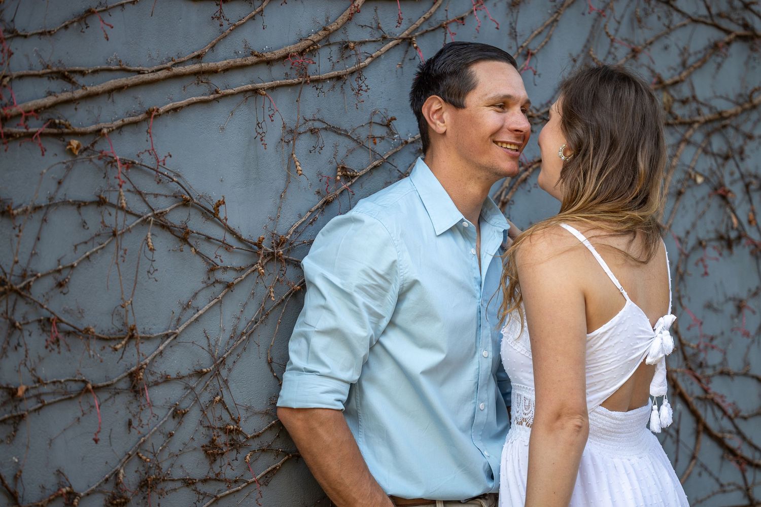A couple shares a tender moment leaning against a vine-covered gray wall.