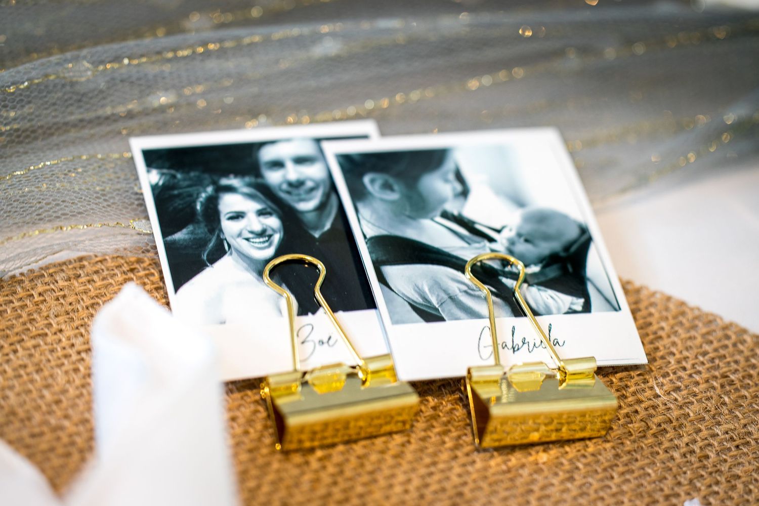 Black and white polaroid photos of wedding couple displayed with gold binder clips on burlap.