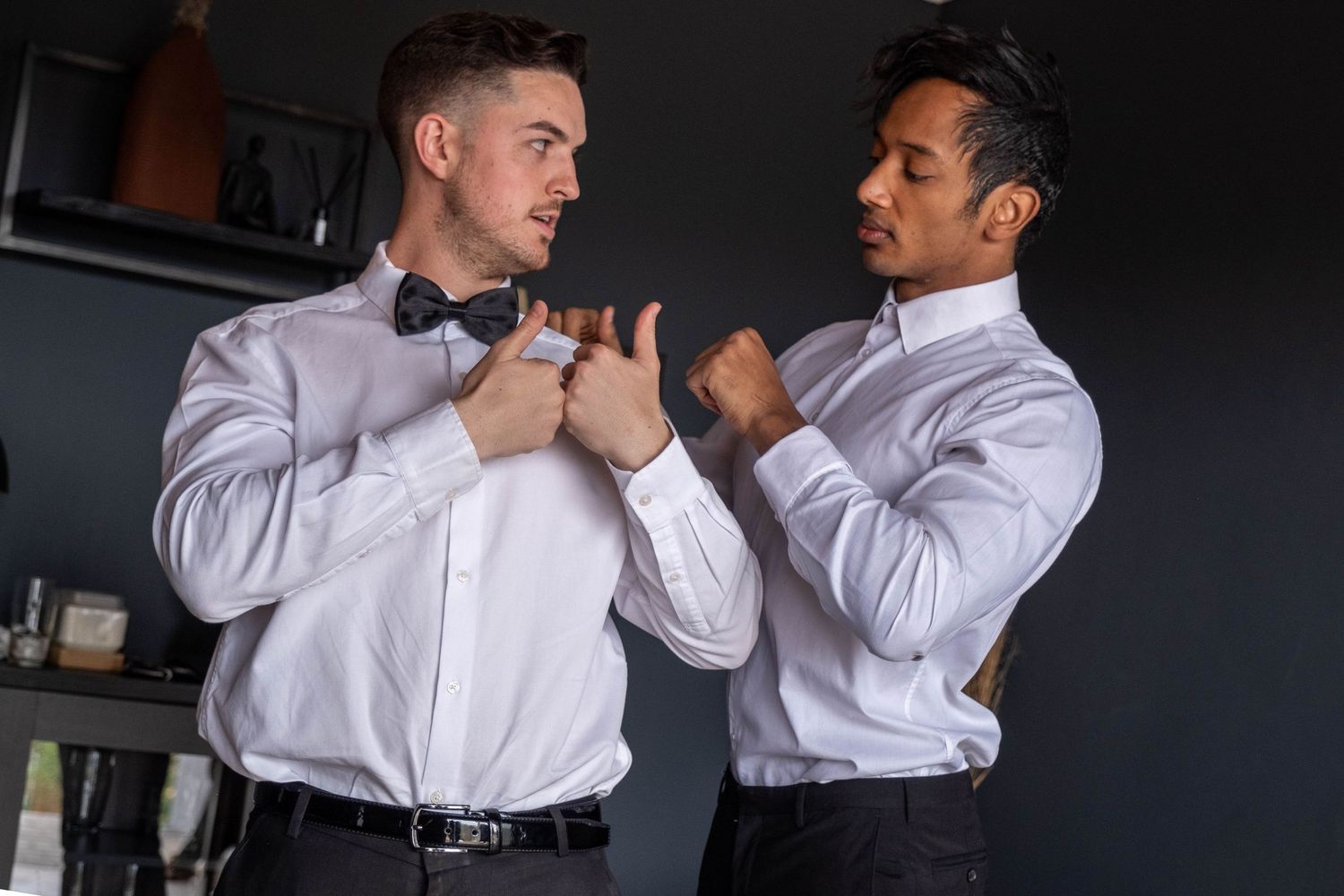 Two men adjusting bow tie and shirt collar while getting dressed together.