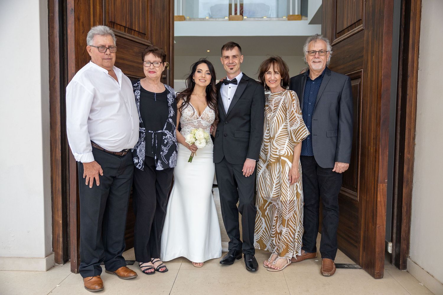 A wedding couple poses with four family members in front of large wooden doors after their ceremony.