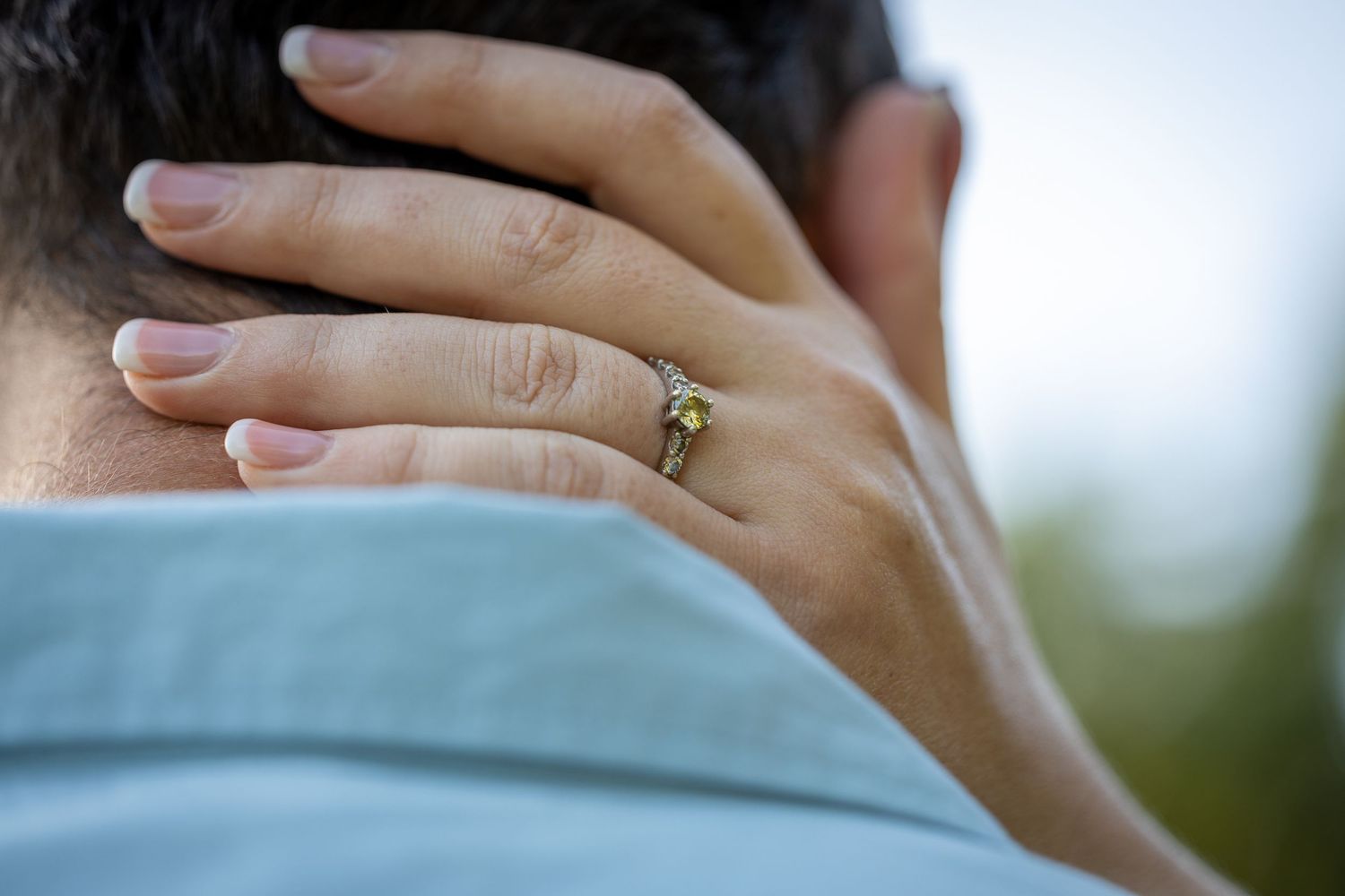 Close-up of womans hand with diamond engagement ring resting on mans neck.