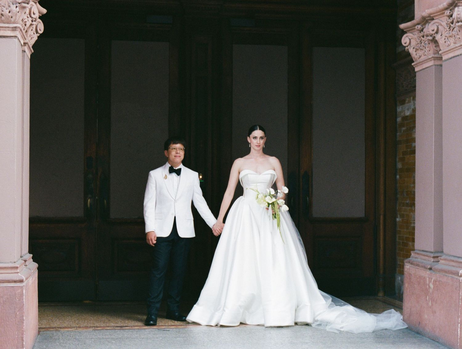 Elegant wedding ceremony scene with white formal attire and decorative architectural elements in the background.