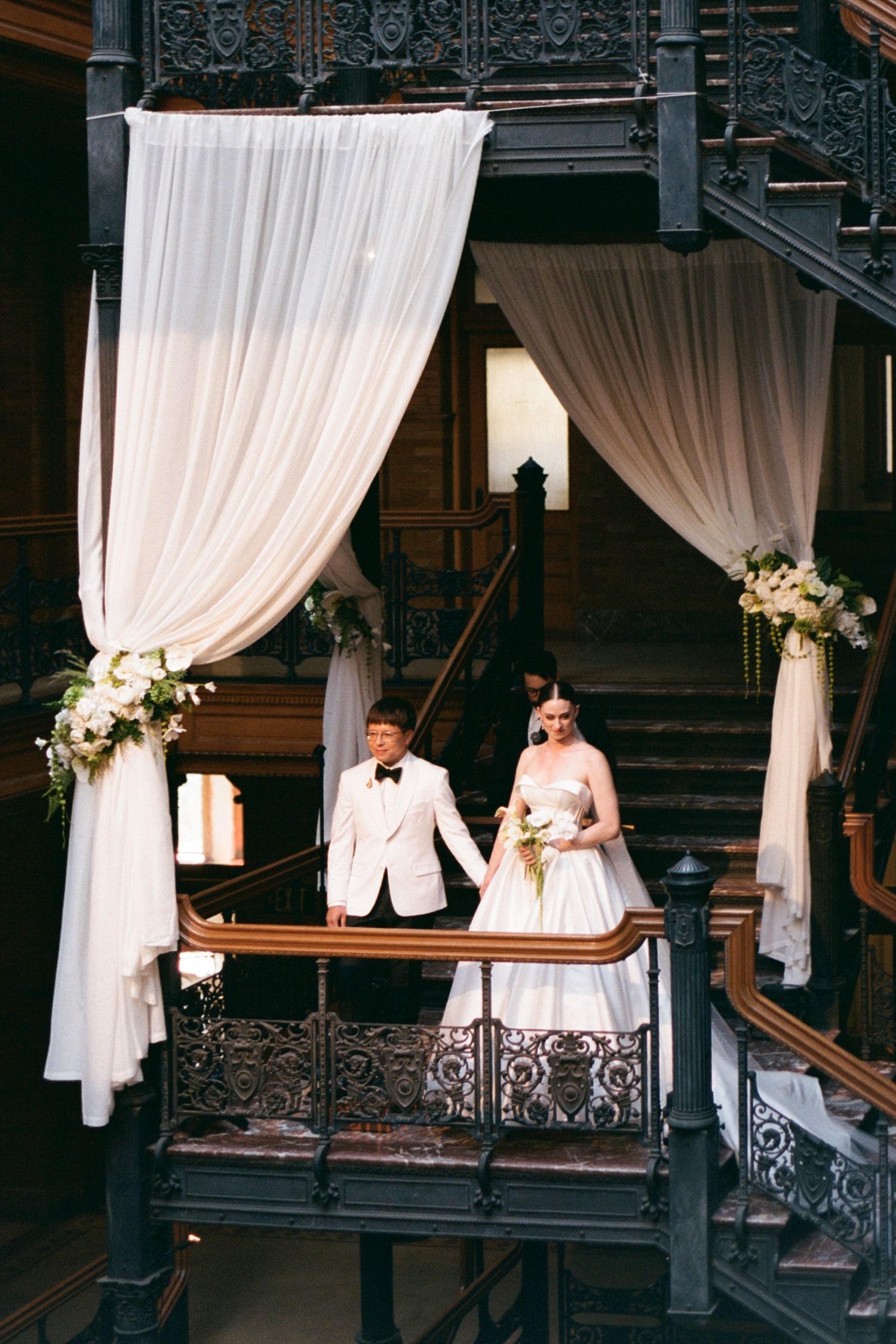 Wedding scene with white drapes and ornate railings in an indoor venue.