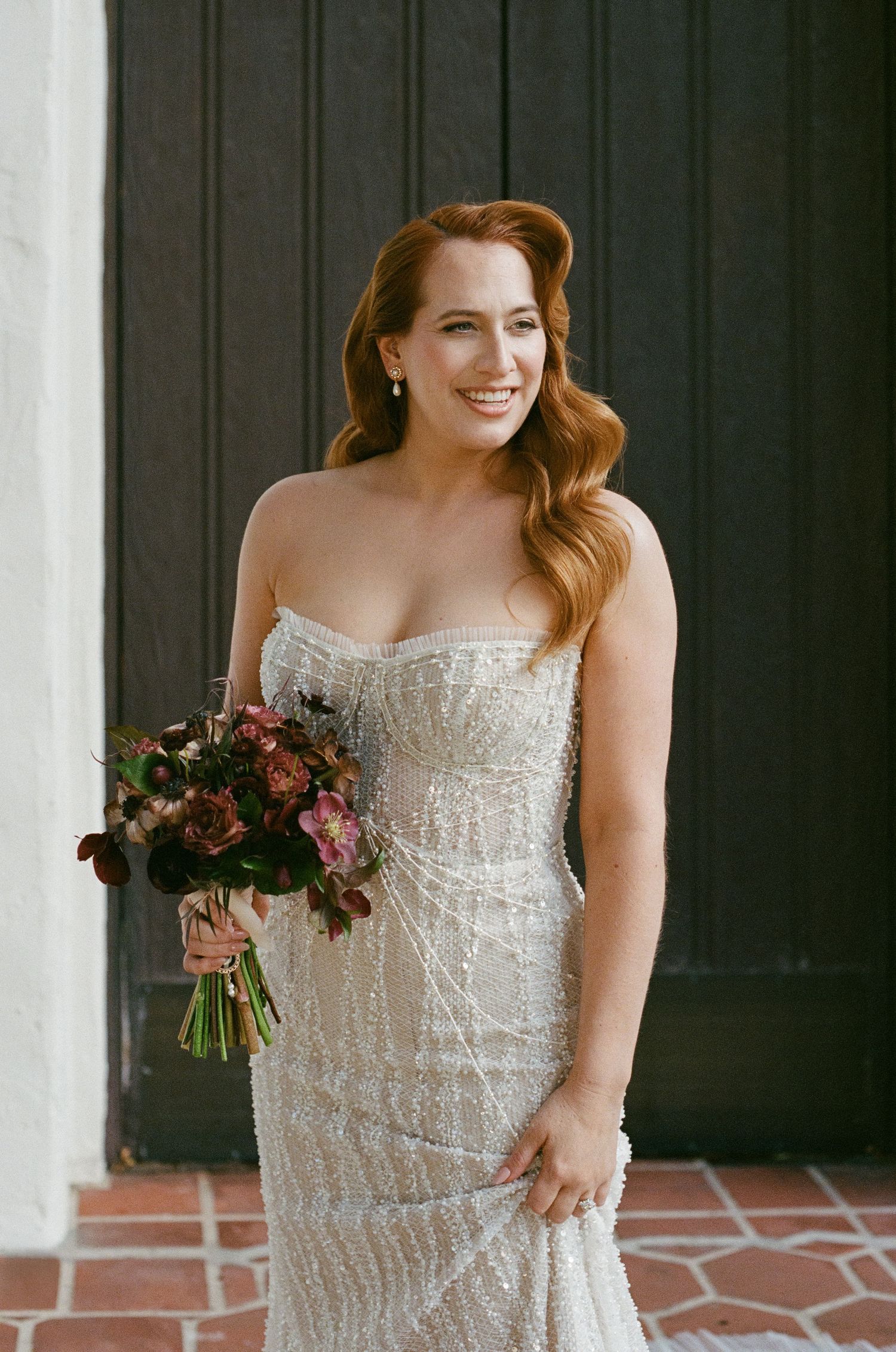Elegant bride in a beaded strapless gown holding a burgundy and pink bouquet.