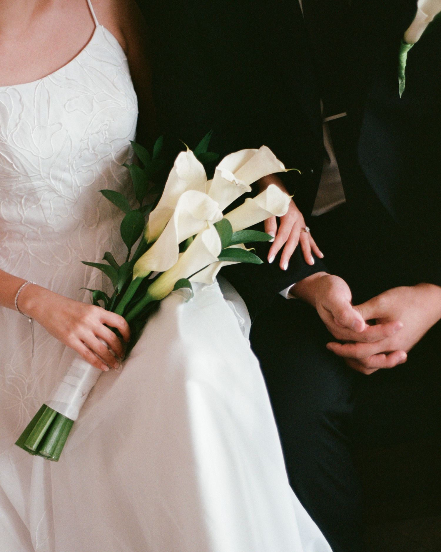 Close-up of white calla lily bouquet held against white wedding dress.