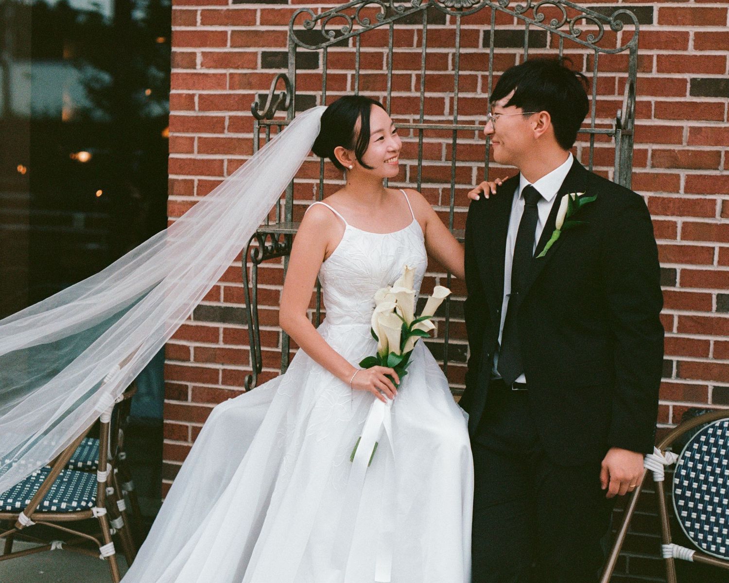 Wedding scene against red brick wall with flowing white veil.