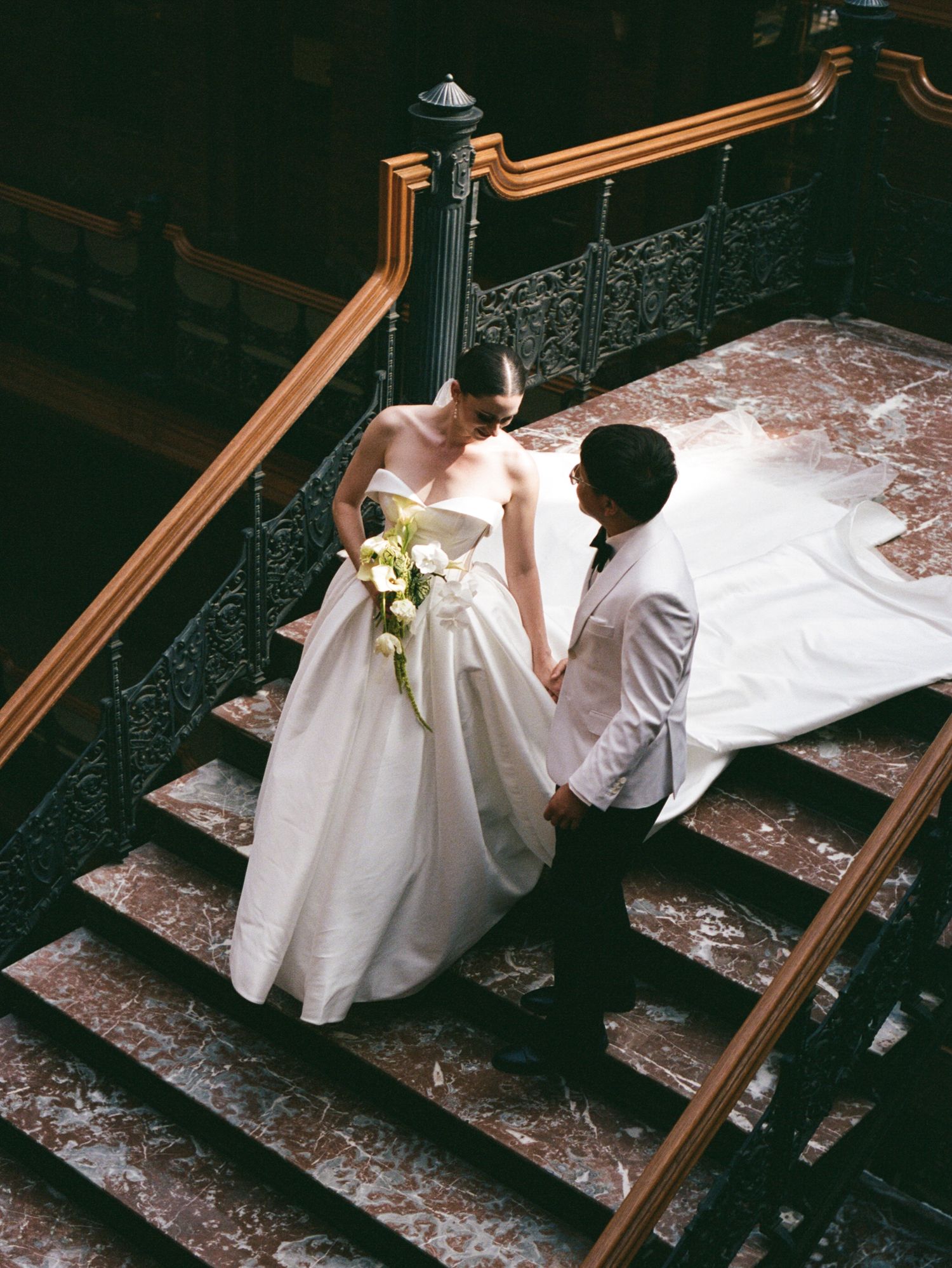 Bride and groom share romantic moment on ornate marble staircase during wedding photoshoot.