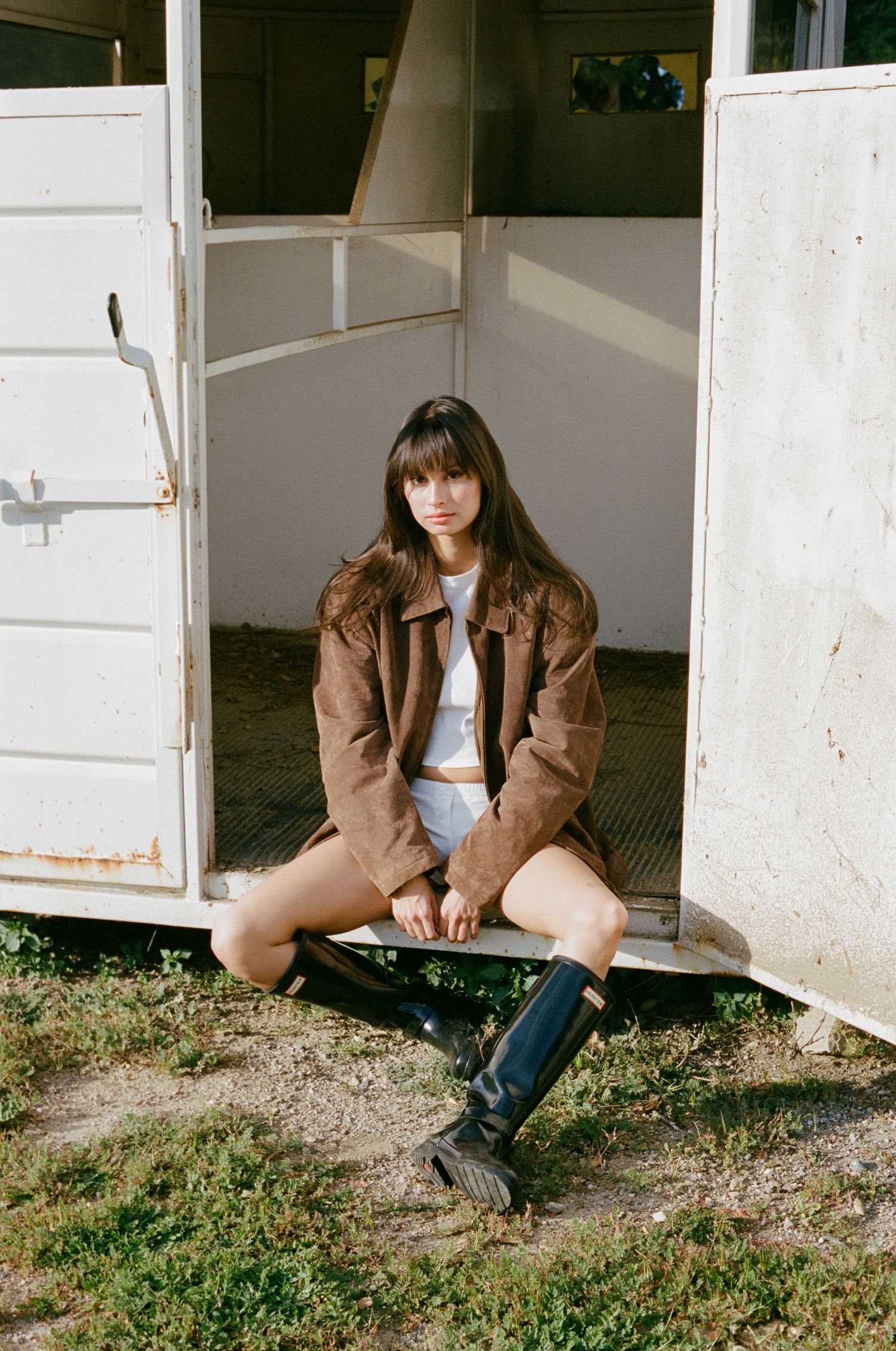 Fashion shoot featuring brown jacket and boots against rustic stable setting.