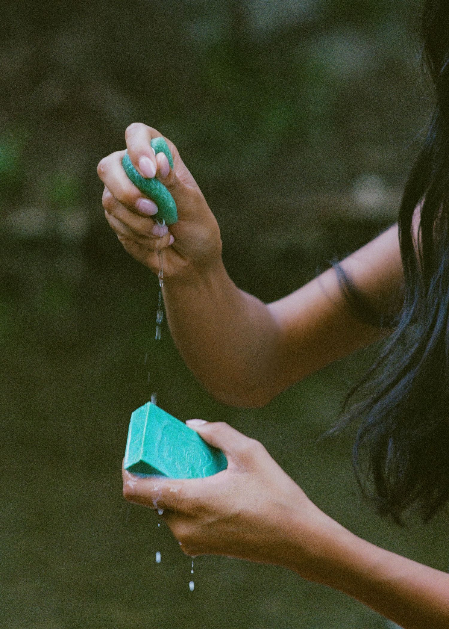 Hands pouring turquoise liquid from a bottle in an artistic outdoor setting.