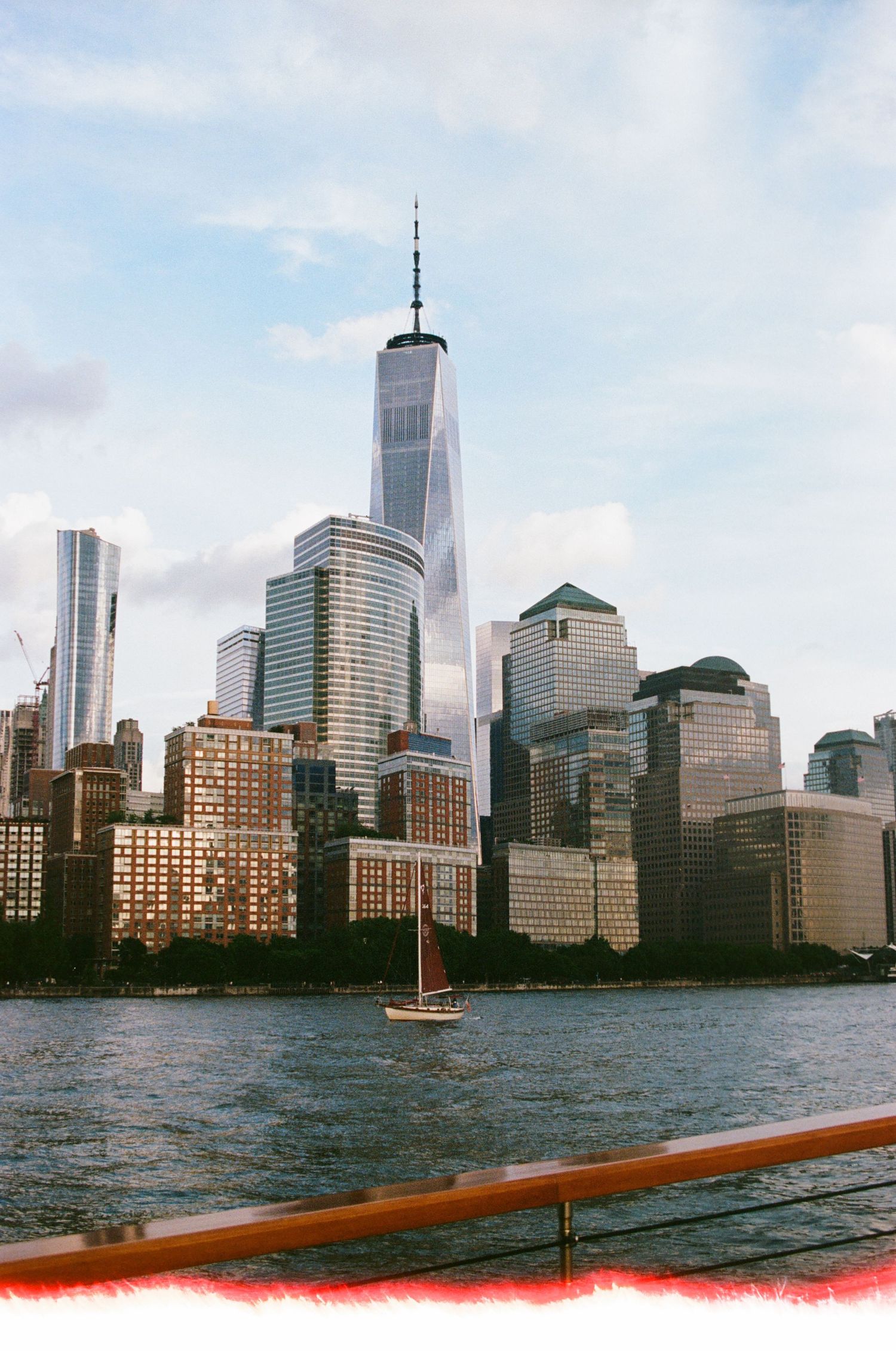 New York City skyline viewed from the water with tall skyscrapers and office buildings against a blue sky.