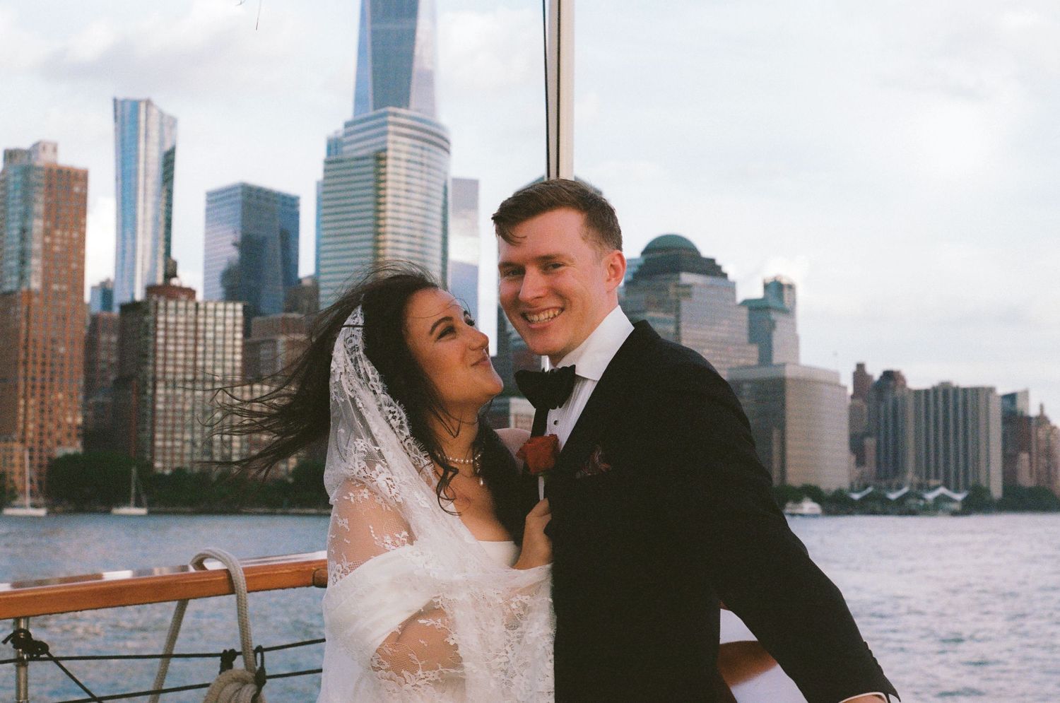 Wedding couple posing with New York City skyline visible across the water.