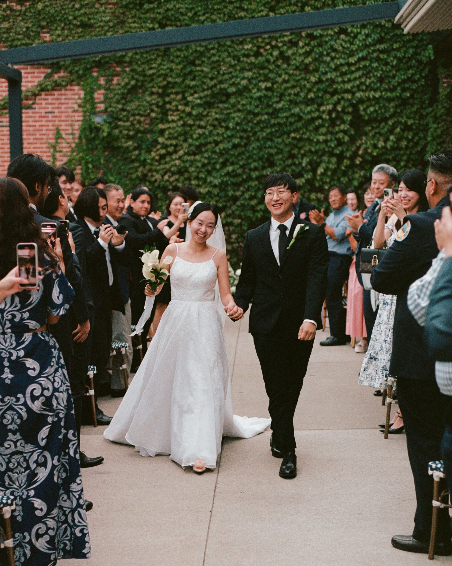 Wedding guests gathered outdoors on patio with ivy-covered walls.