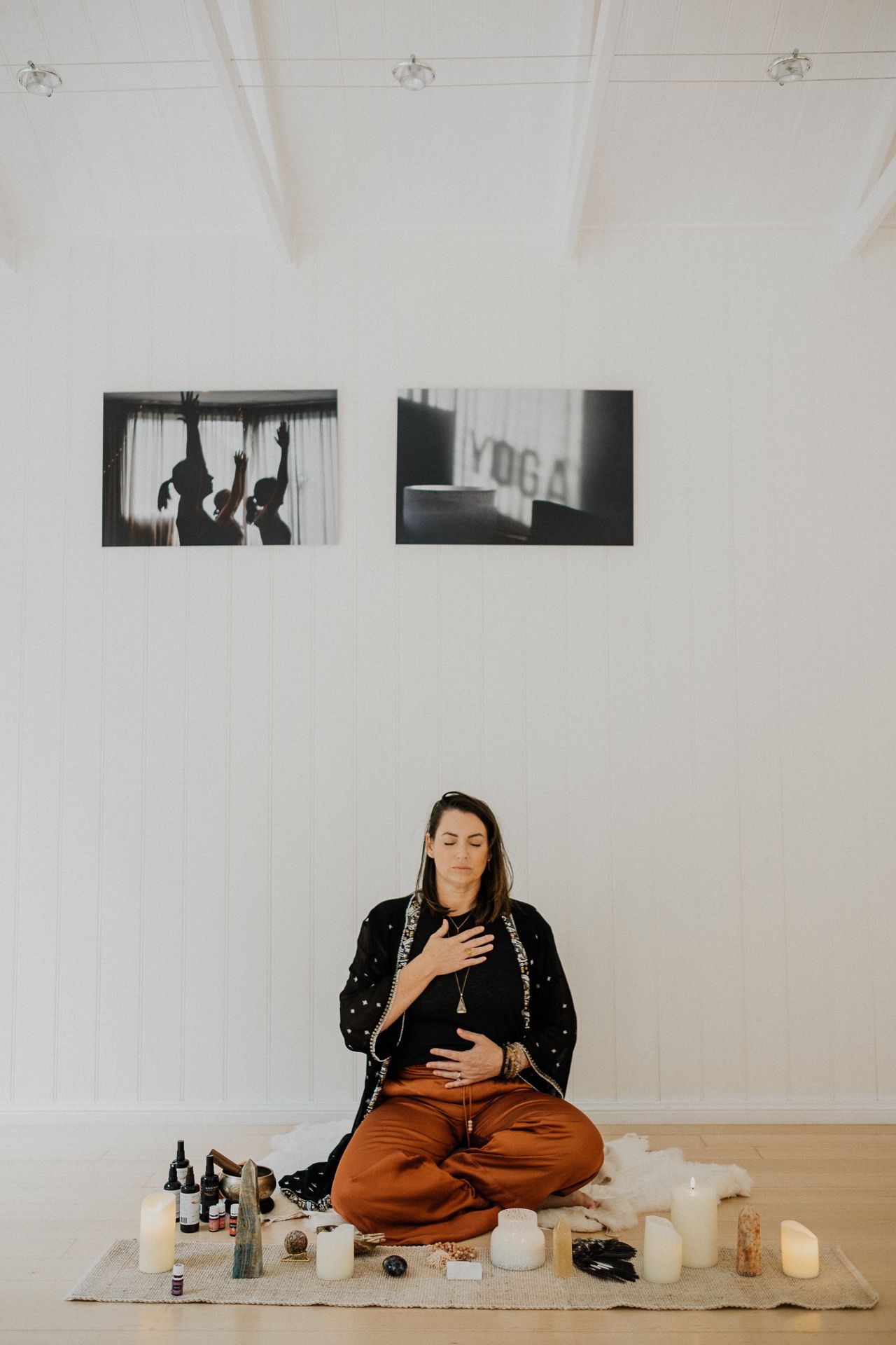 Four minimalist photos show someone sitting on floor with yoga props and crystals in a serene white studio space.