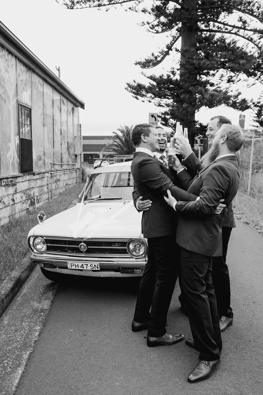 Vintage black and white sequence shows two men in suits engaged in a playful scuffle next to a parked car.