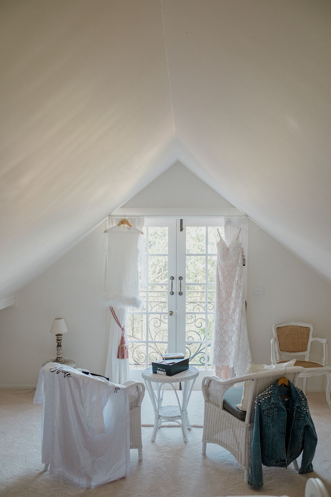 A minimalist white attic room with sloped ceilings, windows, and scattered furniture pieces creates a bright, airy space.