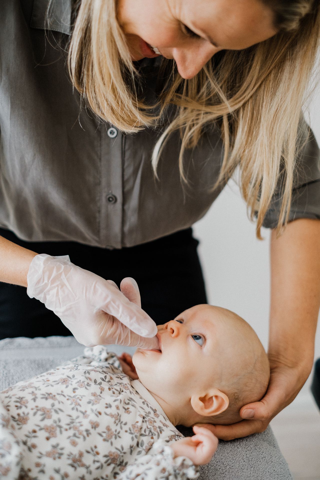 A mother lovingly cares for her baby lying on a floral blanket in a series of tender moments.