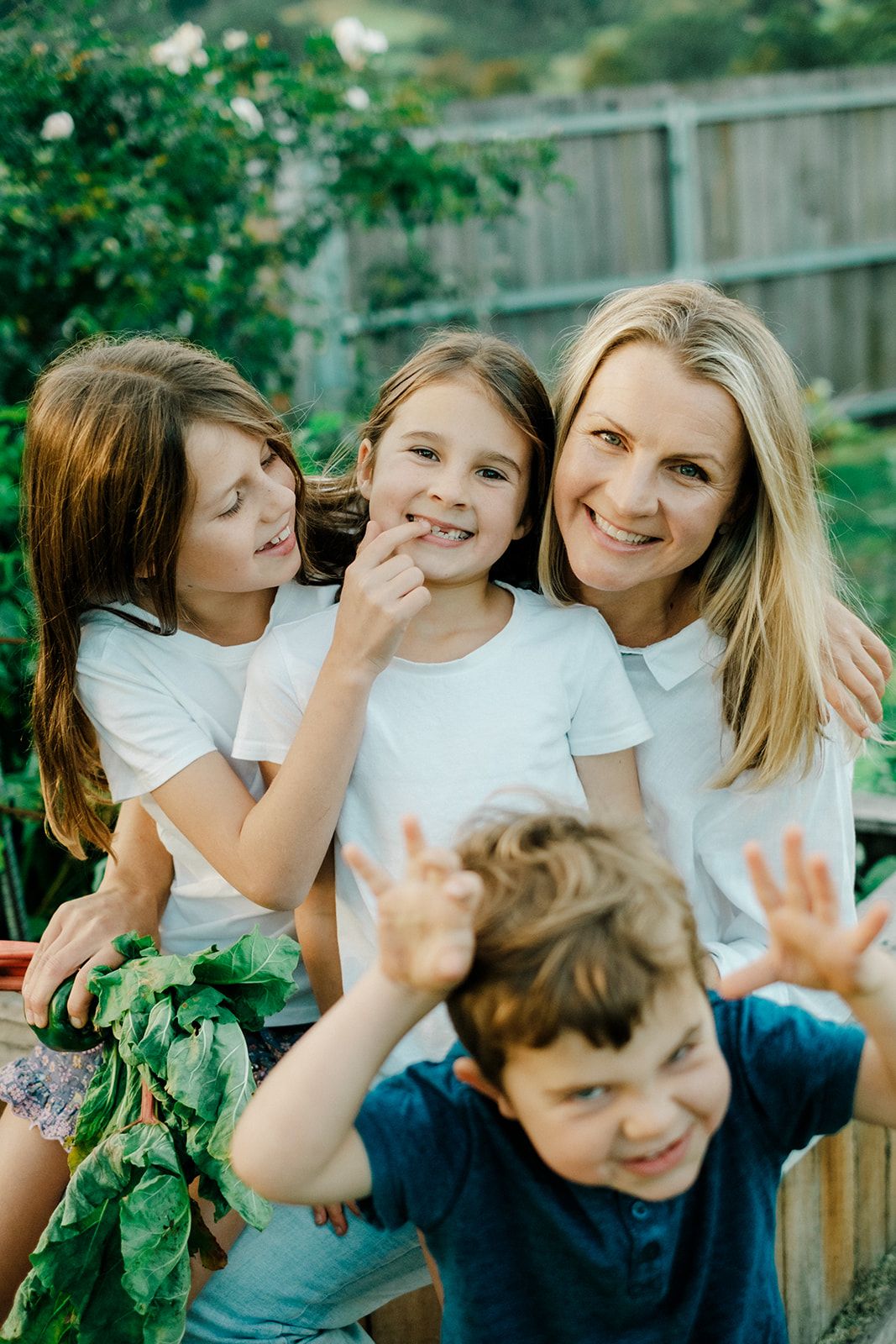 Playful family moment in a backyard garden with white shirts and raised hands near a wooden fence.