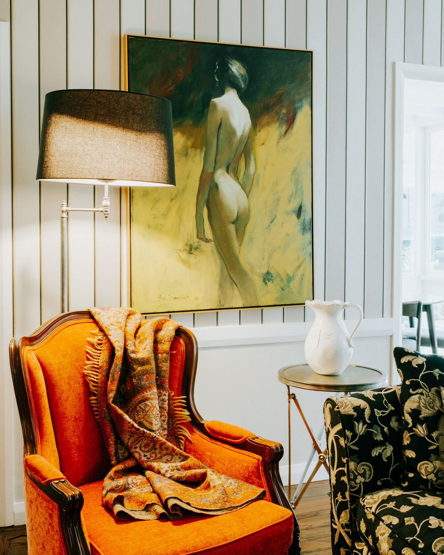 Vintage brown cowboy boots displayed on an orange velvet chair against white paneled walls with artwork.
