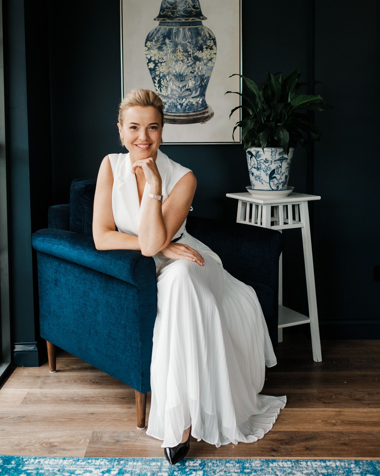 A person in a white dress sits on a blue velvet couch in an elegant room with blue and white decor.