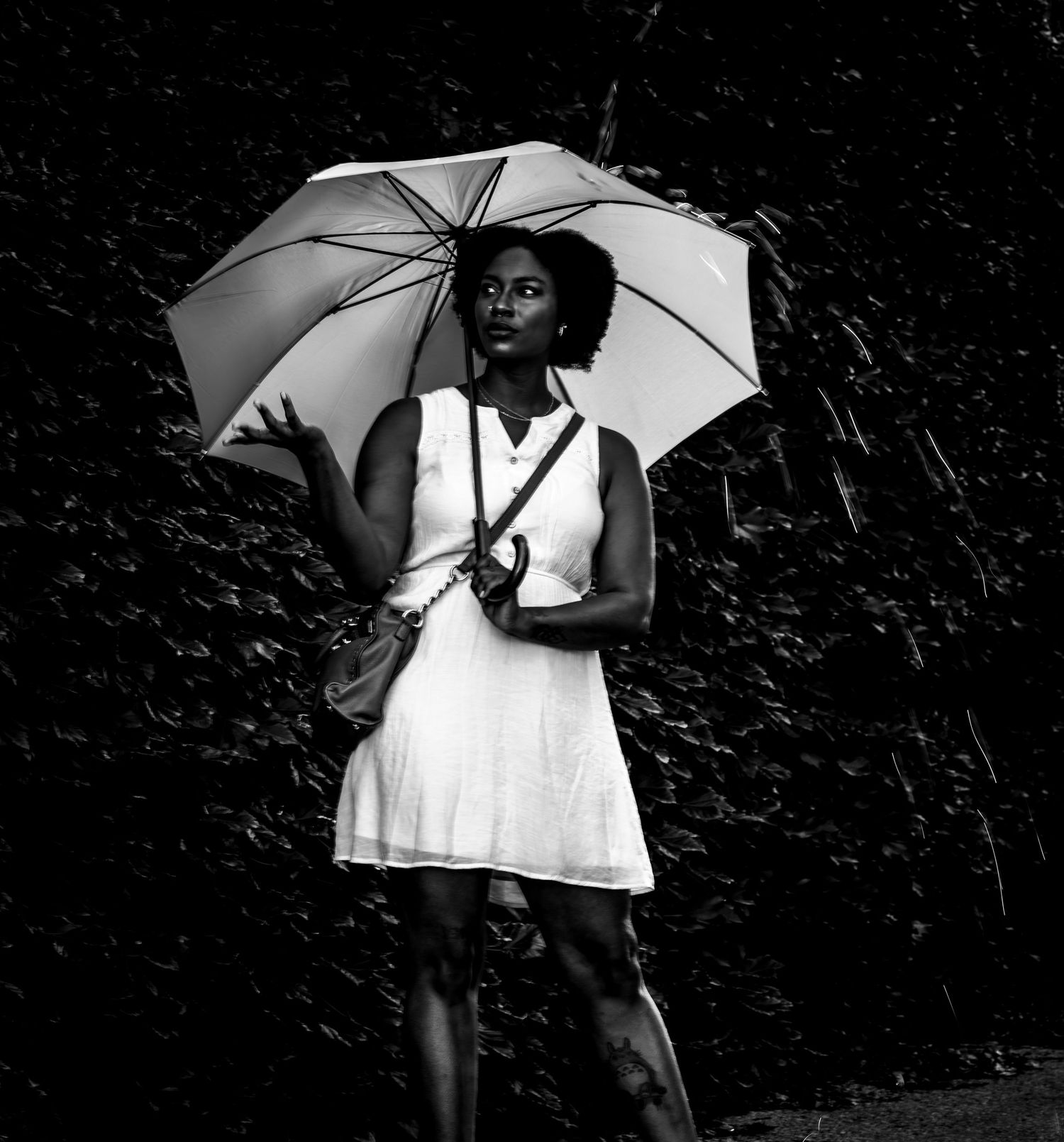 A person in a white dress holds a white umbrella while standing against a dark background in black and white.