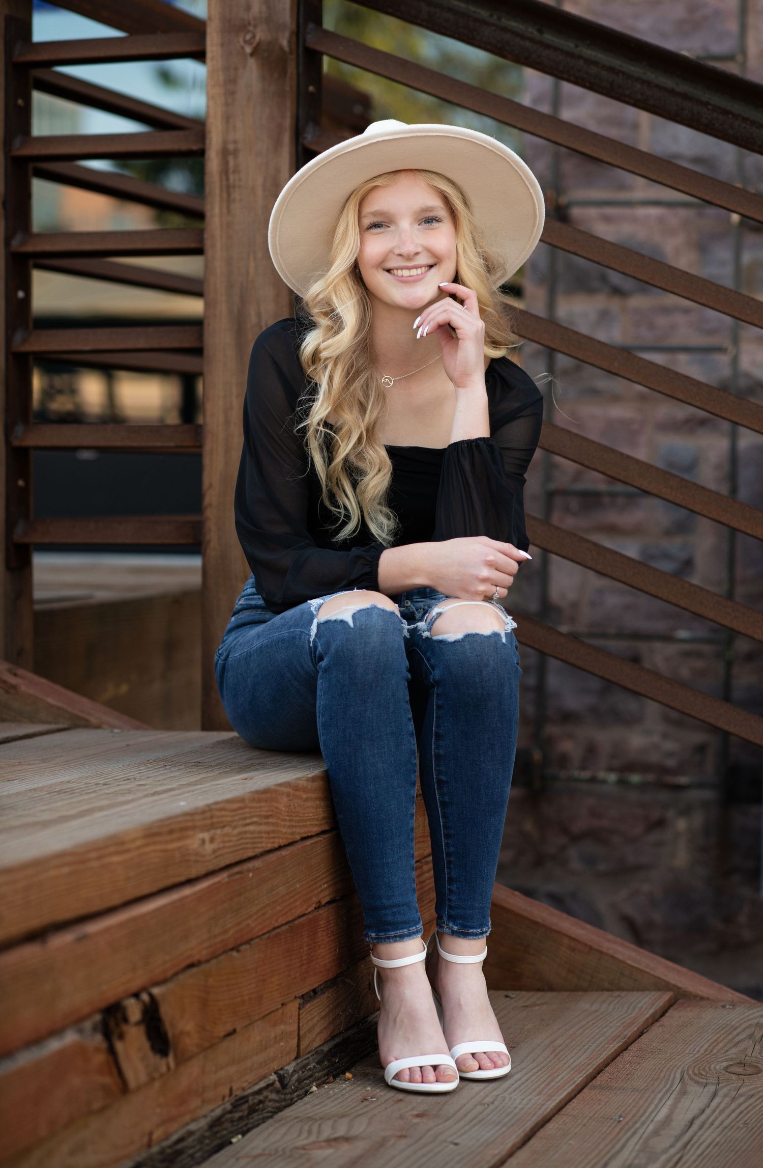 Woman in hat and black top sits casually on wooden steps outdoors.