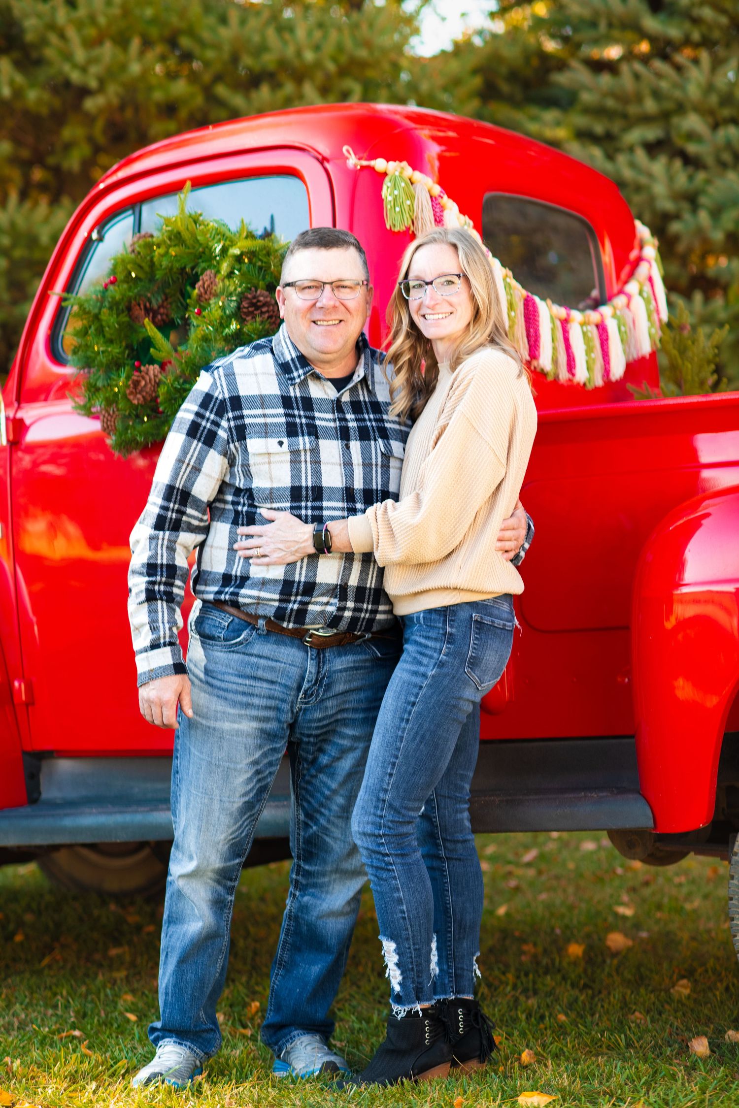 A red vintage truck decorated with holiday greenery serves as a backdrop for a fall photo.