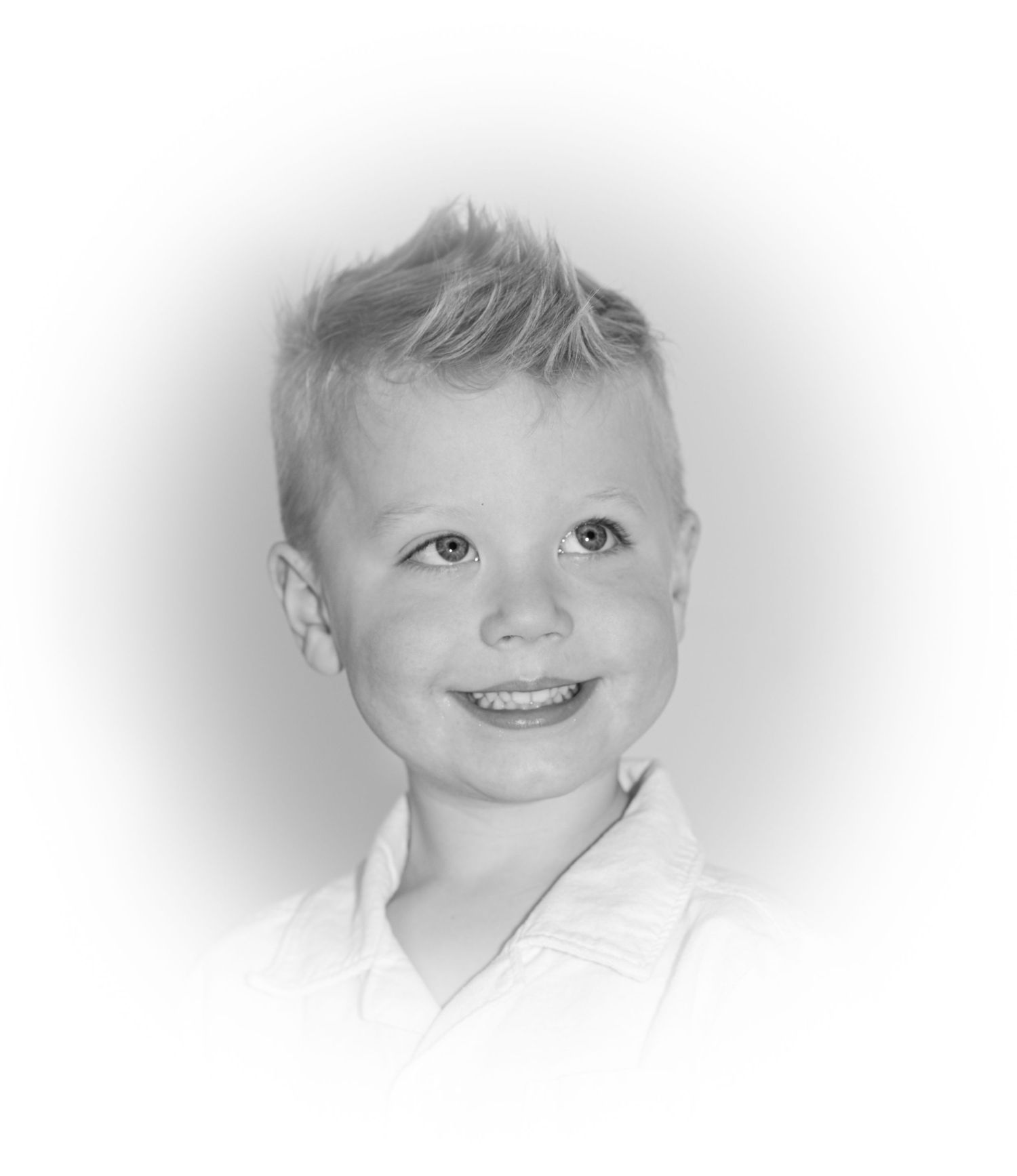 Black and white headshot of smiling young child with short hair against light background.
