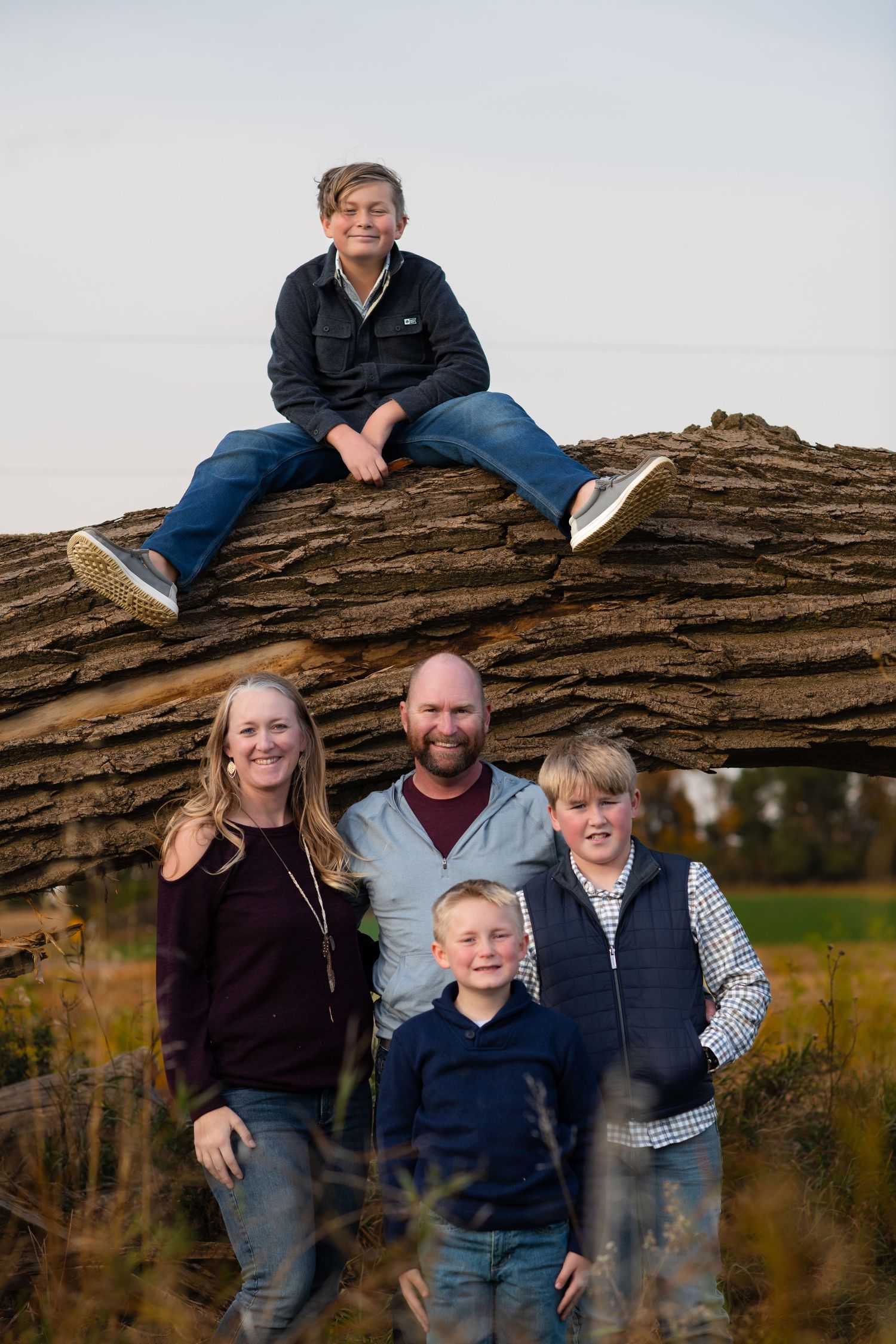 Family poses near large fallen log outdoors with natural backdrop.