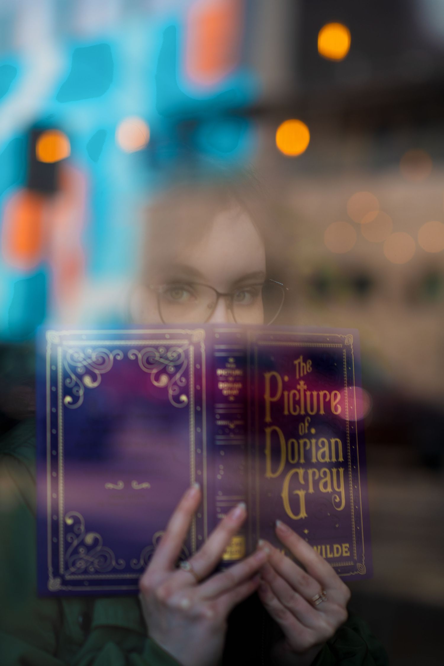 Hands holding copy of The Picture of Dorian Gray book with bokeh lights in background.