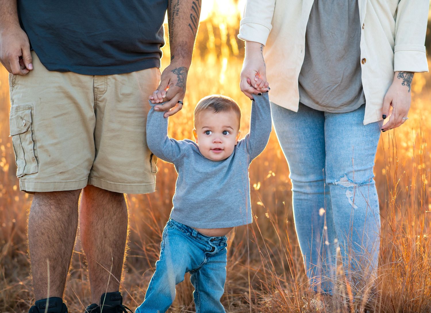 Small child in blue shirt walks while holding hands in golden field at sunset.