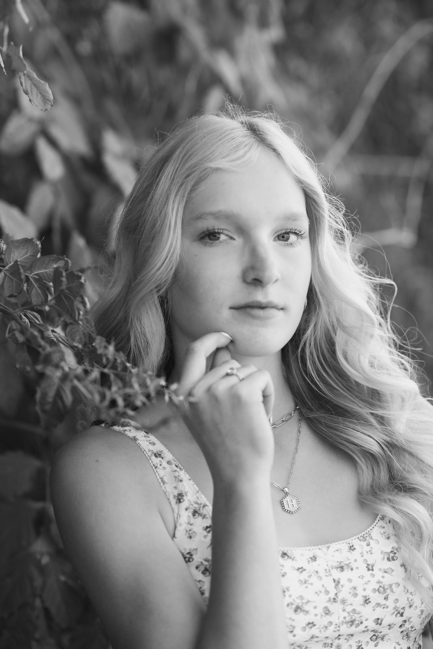 A portrait in black and white featuring soft lighting and natural foliage background.