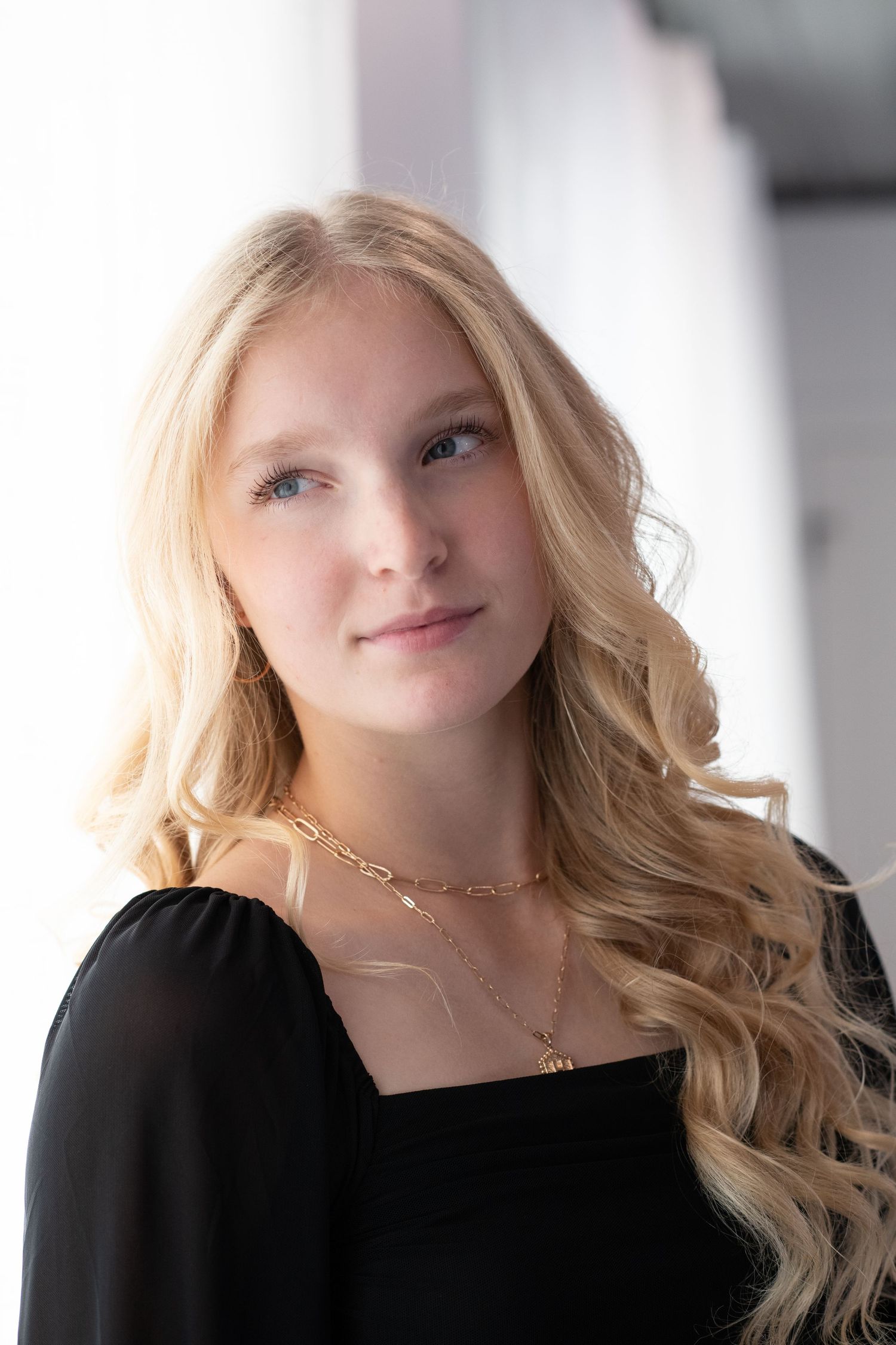 Portrait of a woman with long blonde hair wearing a black top and delicate gold necklaces.