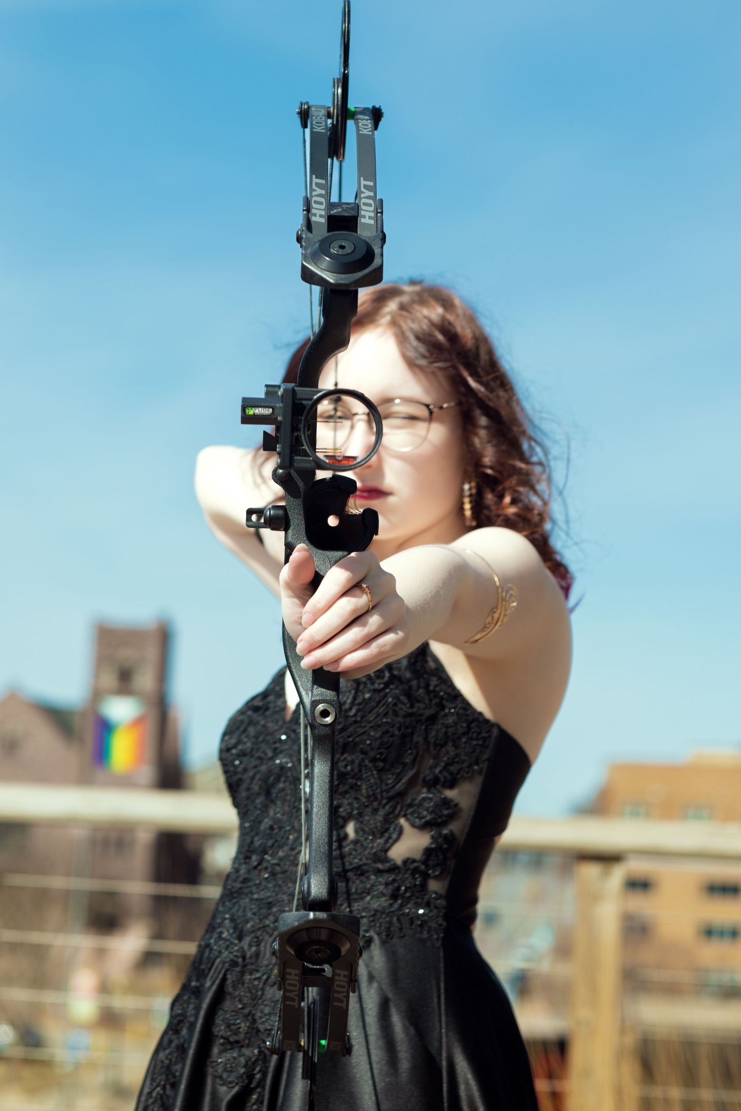Woman in black dress aims sextant instrument against urban rooftop backdrop.