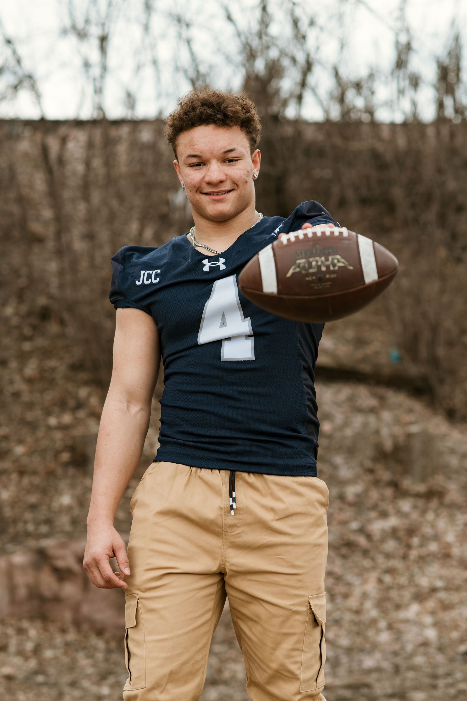 Football player in navy jersey holds ball while posing for athletic portrait.