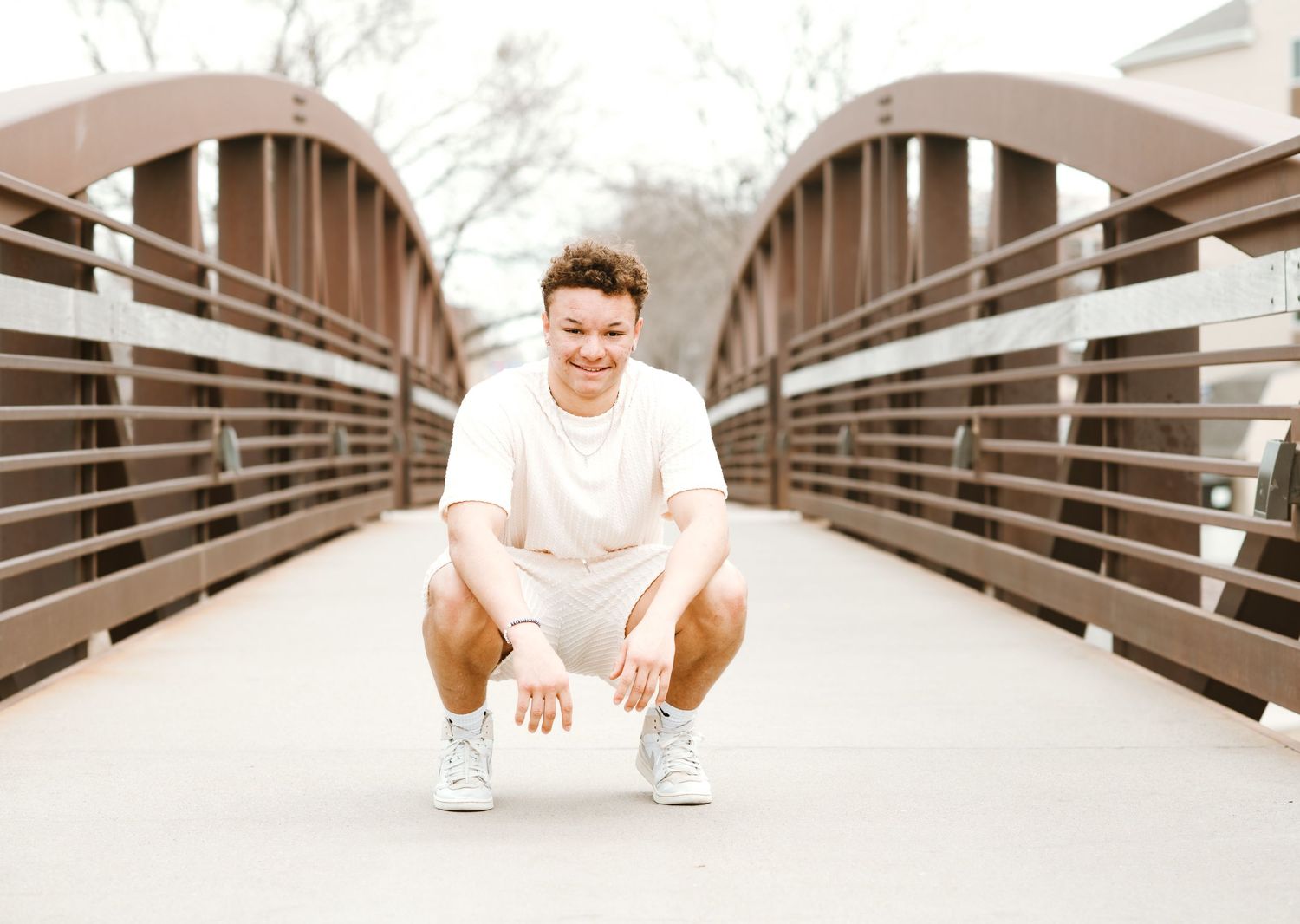 Person in white outfit crouching on wooden bridge with curved arches.