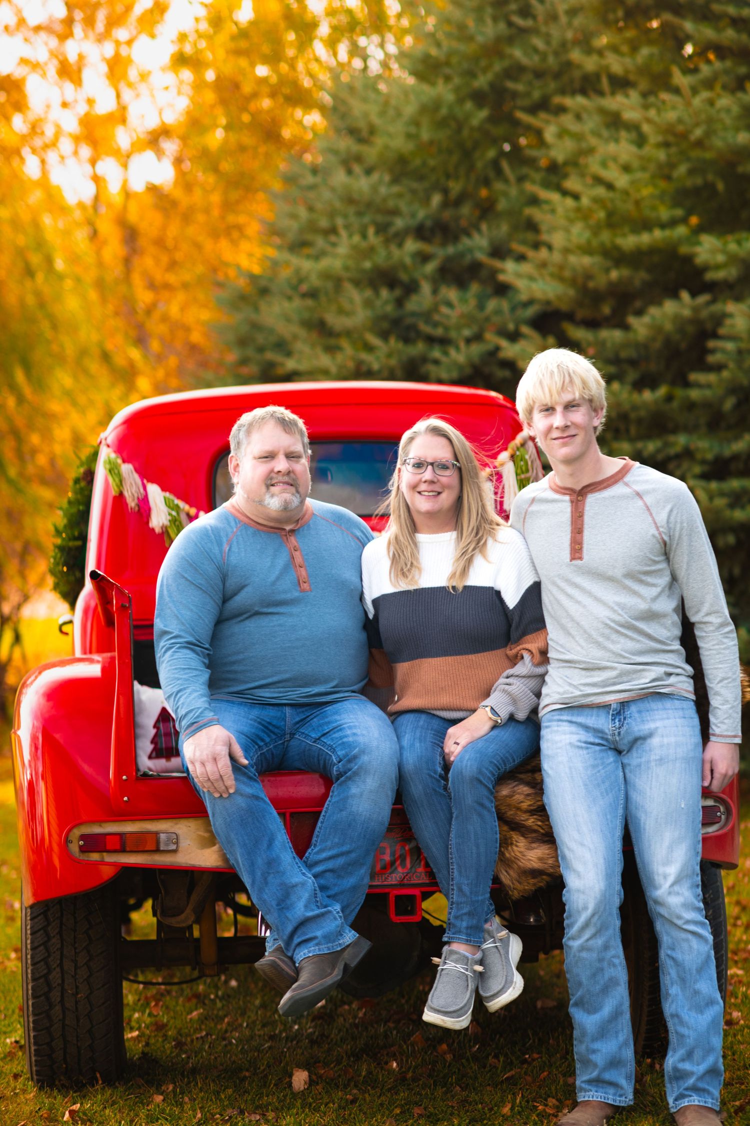 People sitting together on the tailgate of a vintage red pickup truck during golden autumn sunset.